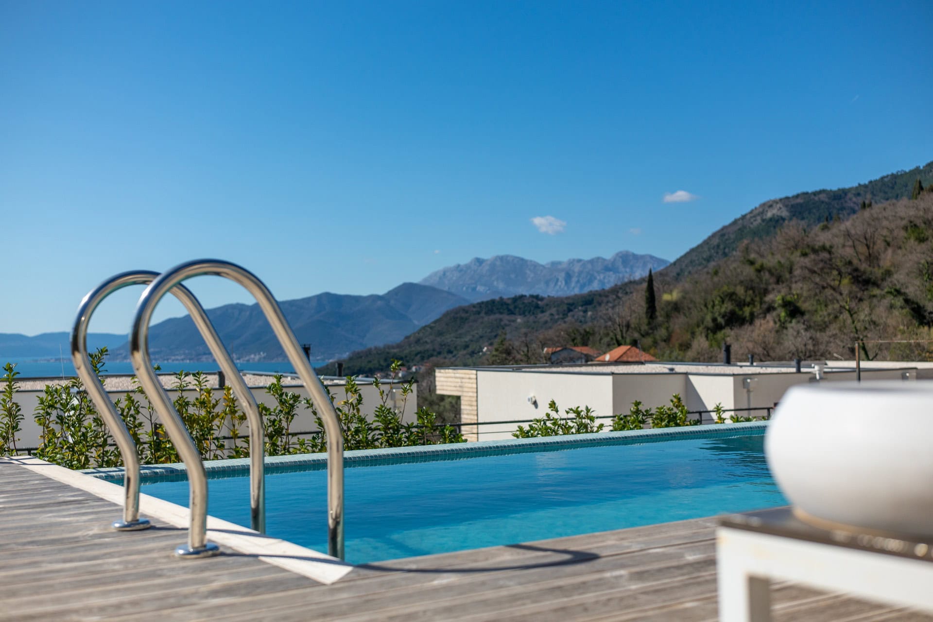 An outdoor pool with mountain and sea views at a villa in Kavac, Montenegro, with a wooden terrace and modern finishes.