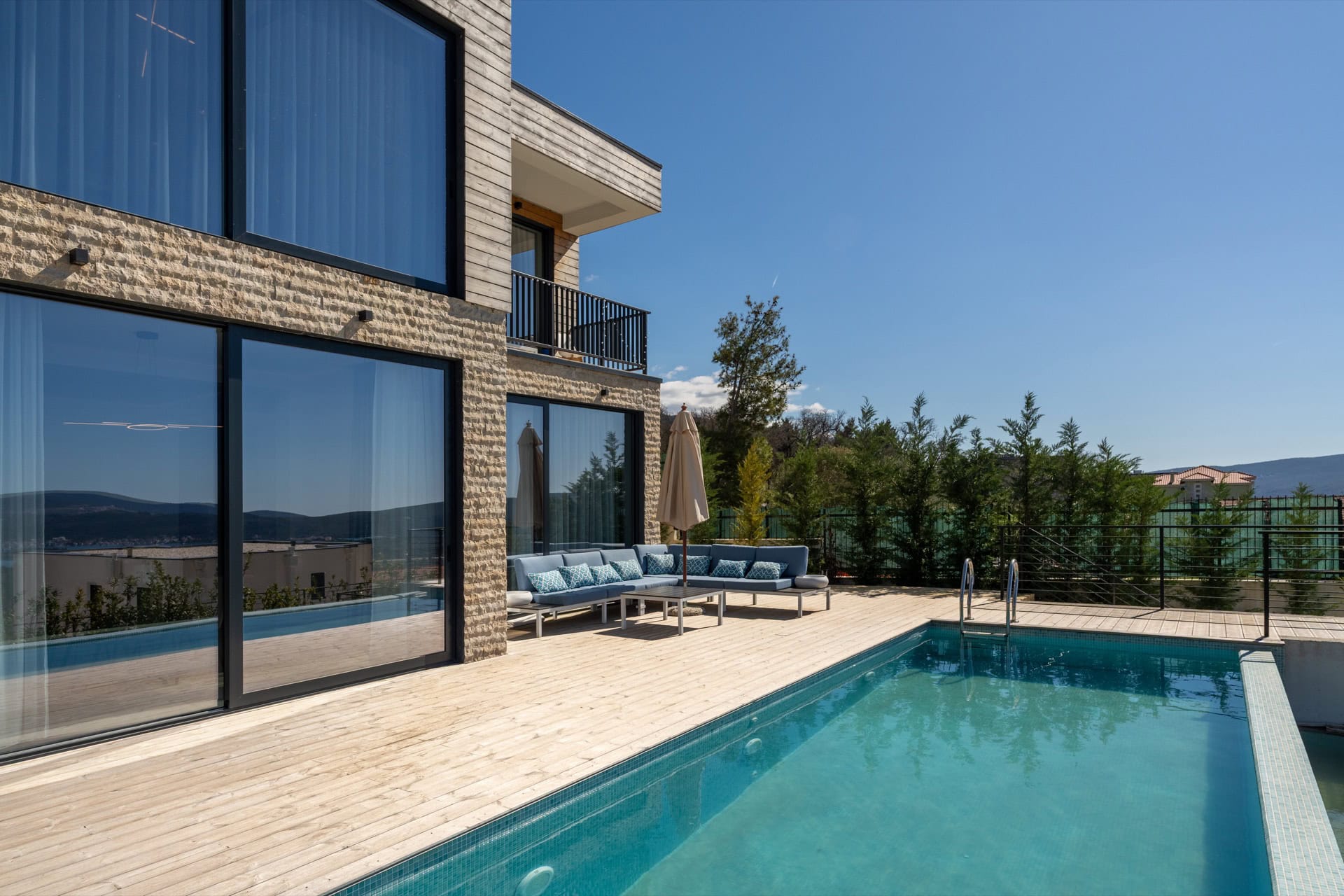 Modern villa in Kavac, Montenegro: terrace with a pool, lounge area with soft seating, and panoramic glazing.