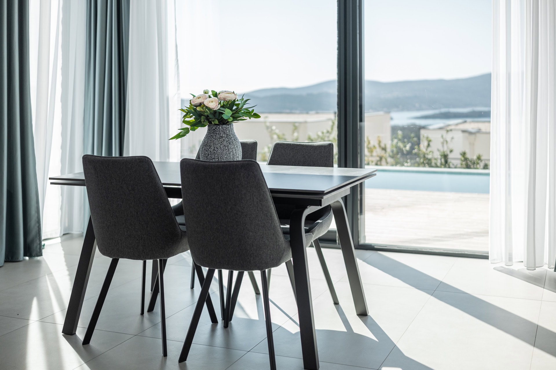Dining area with panoramic sea and pool views in a villa in Kavac, Montenegro: stylish furniture and a bright interior.