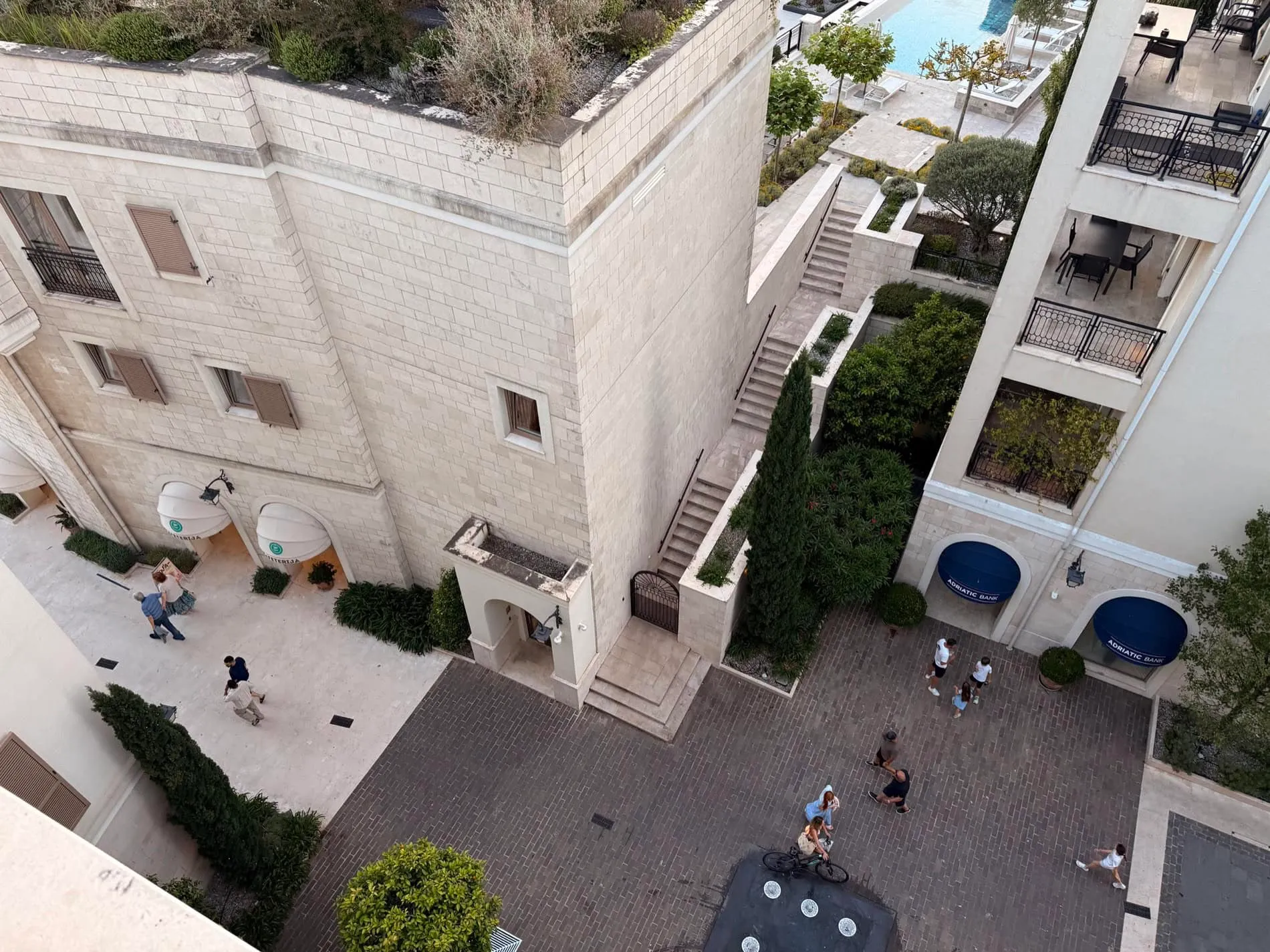 Blick von oben auf den Wohnkomplex Porto Montenegro in Tivat, Montenegro: Steinfassaden, Fußgängerplatz und Pool.