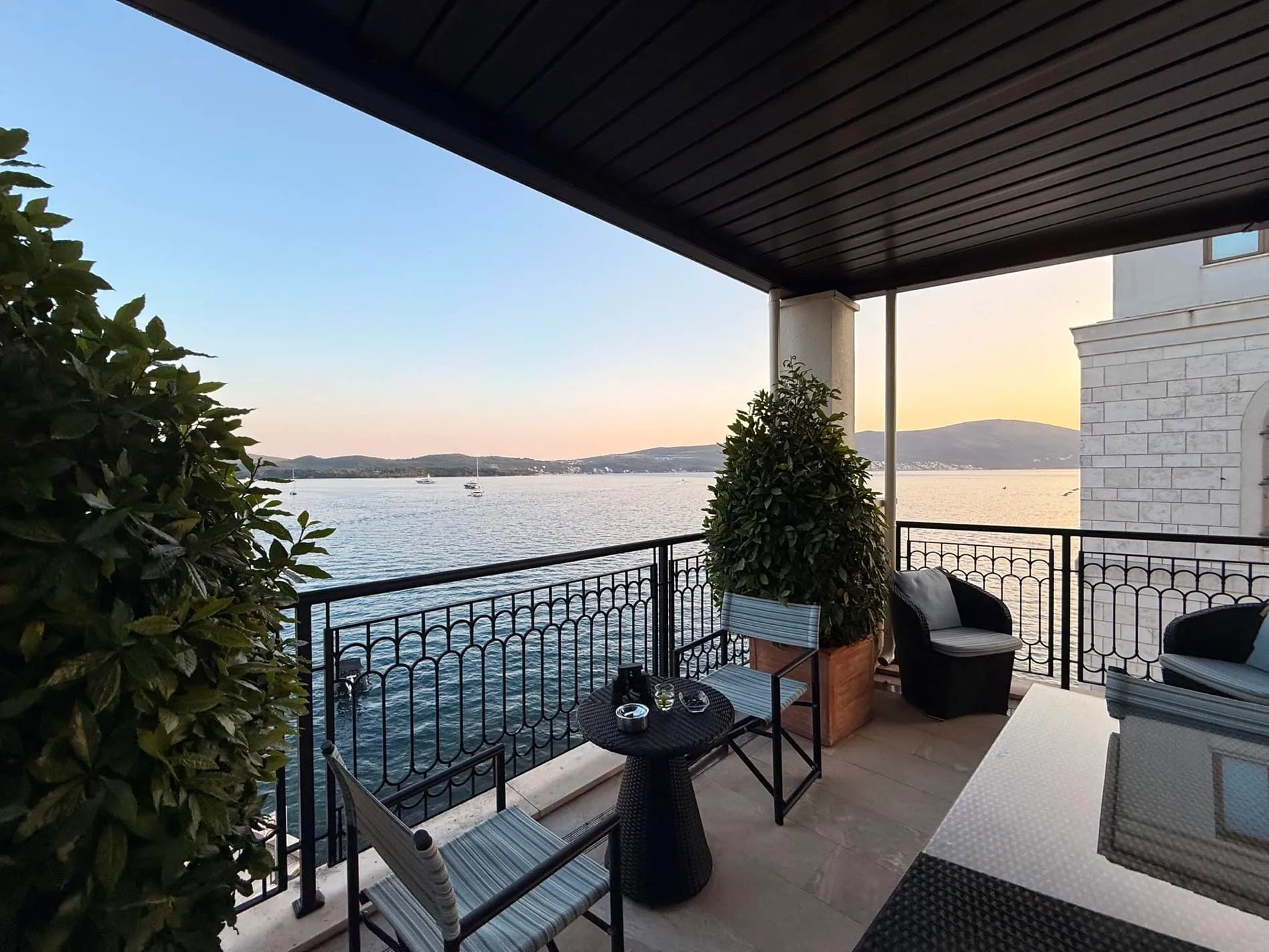 Terrasse mit Rattanmöbeln und Meerblick in einer Wohnung in Tivat, Montenegro. Gemütlicher Balkon mit Überdachung und Pflanzen.