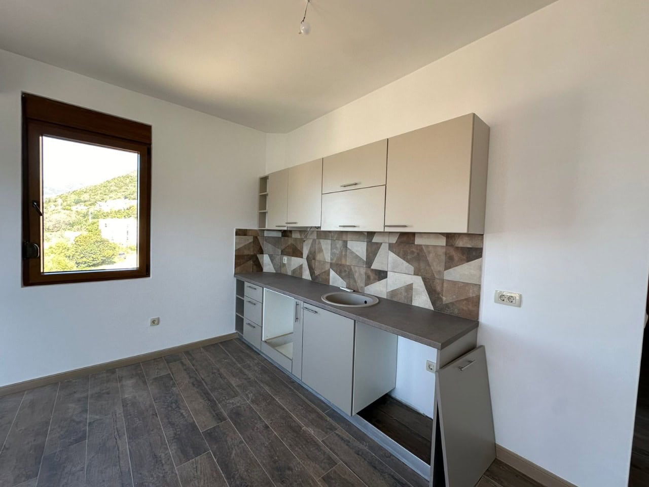 Küche in der Wohnung in Kumbor, Montenegro: helle Einbauküche, Fliesenspiegel mit geometrischem Muster und Bergblick aus dem Fenster.