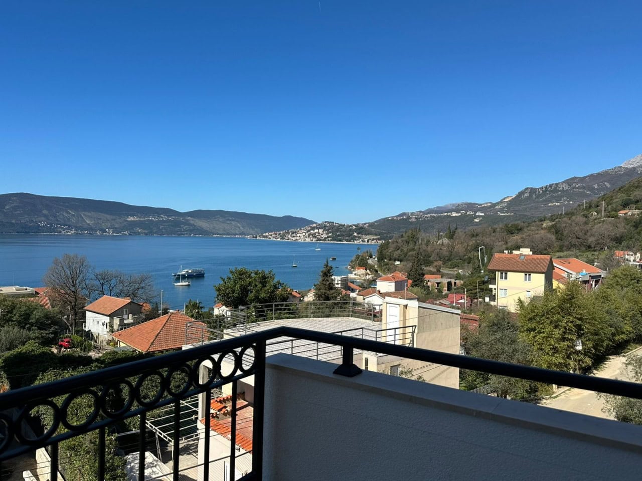 Blick vom Balkon der Wohnung in Kumbor, Montenegro: Panorama auf die Bucht von Kotor, Berge und Küstenhäuser mit Ziegeldächern.