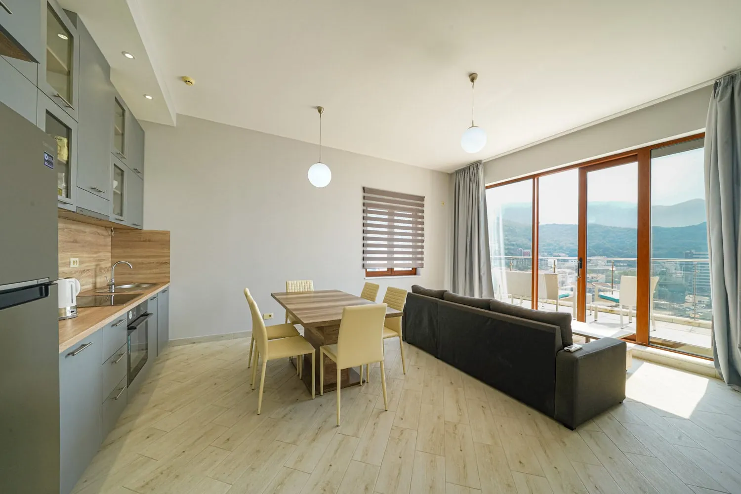 Otwarta sala z kuchnią, stołem jadalnianym, kanapą i dużymi oknami panoramicznymi.