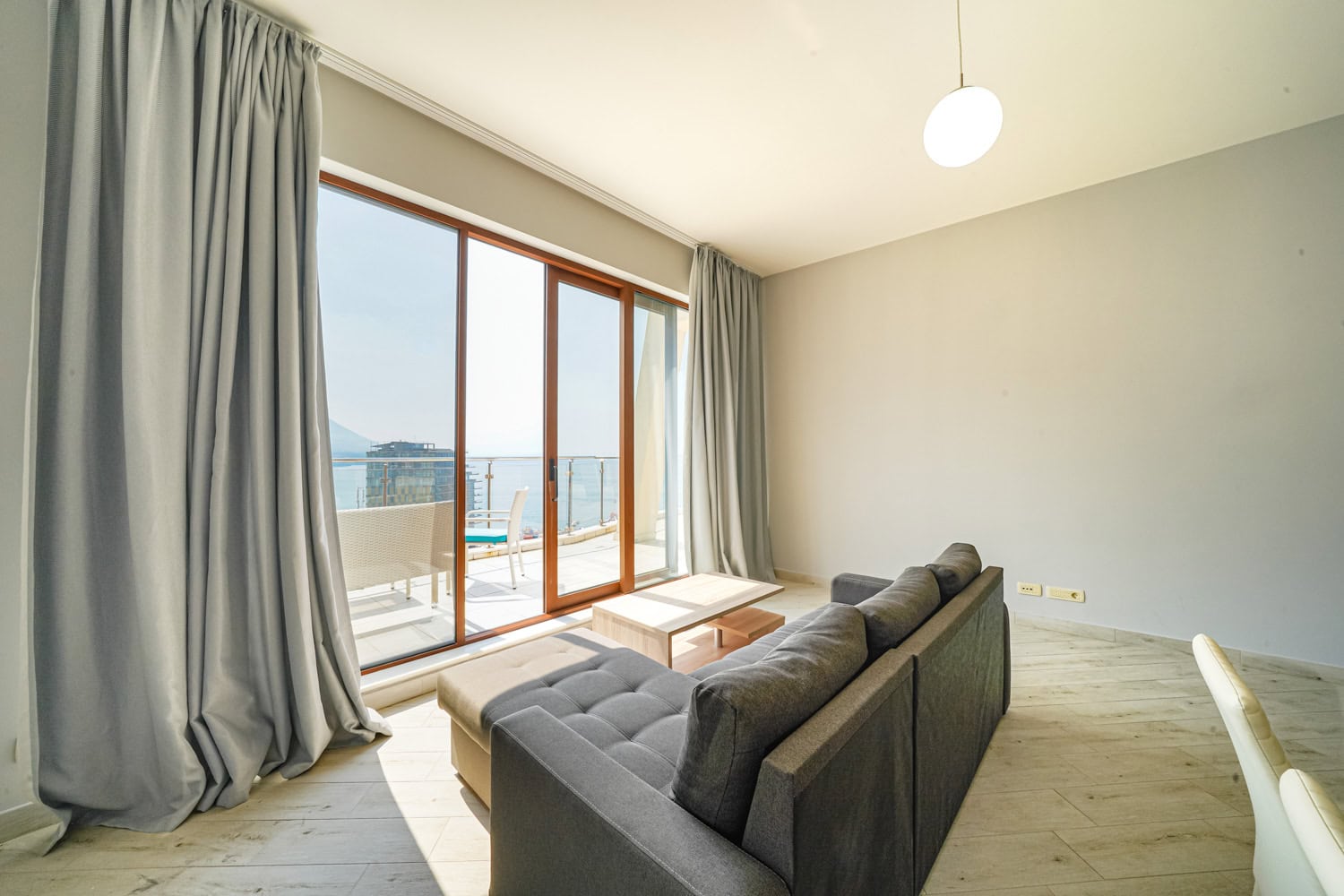 Dnevni boravak sa panoramskim prozorima i pogledom na more u stanu, Bečići, Crna Gora: moderna sofa i izlaz na terasu.