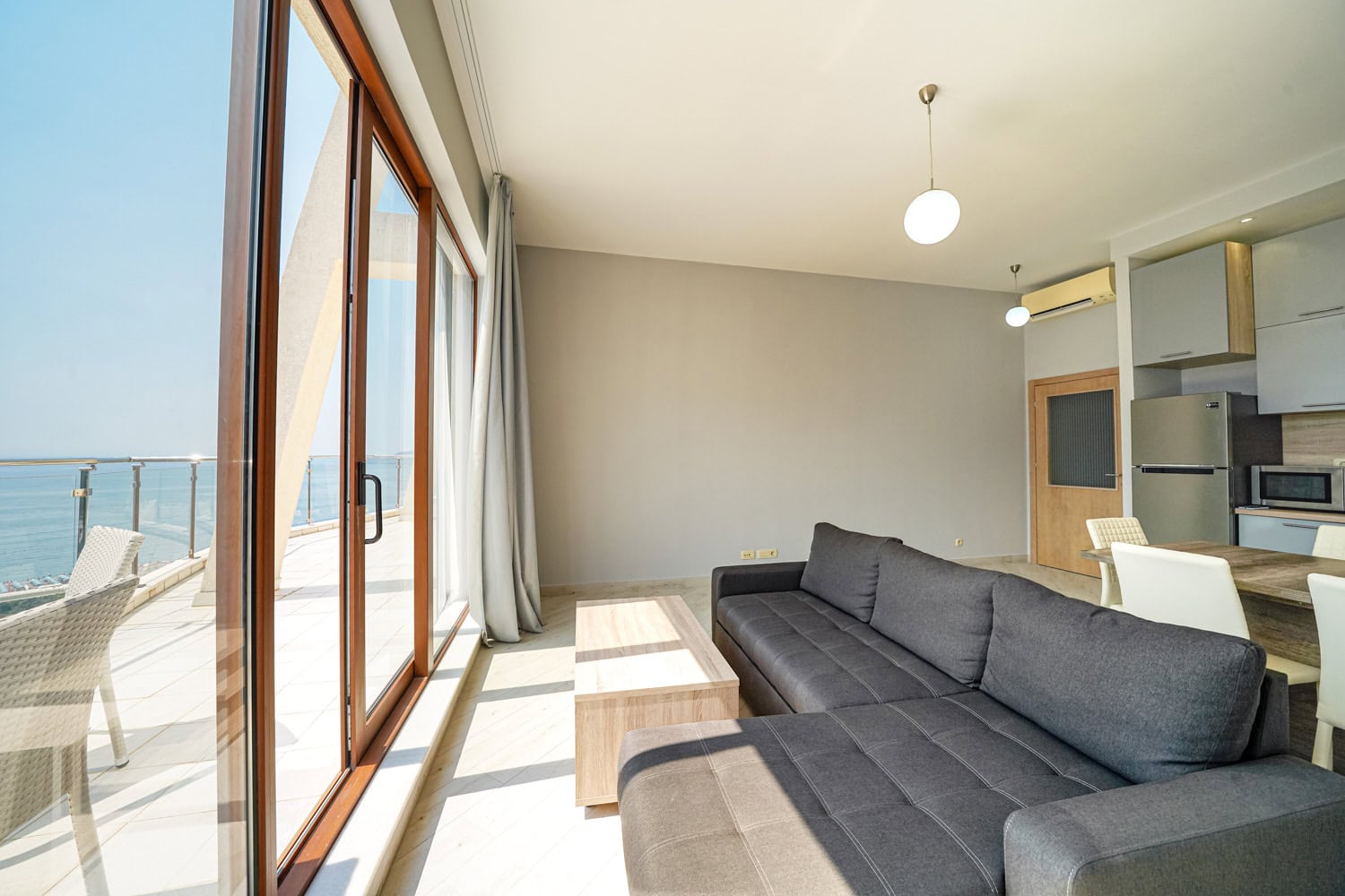 Dnevni boravak sa panoramskim pogledom na more u stanu u Bečićima, Crna Gora: siva sofa, kuhinja i izlaz na terasu.