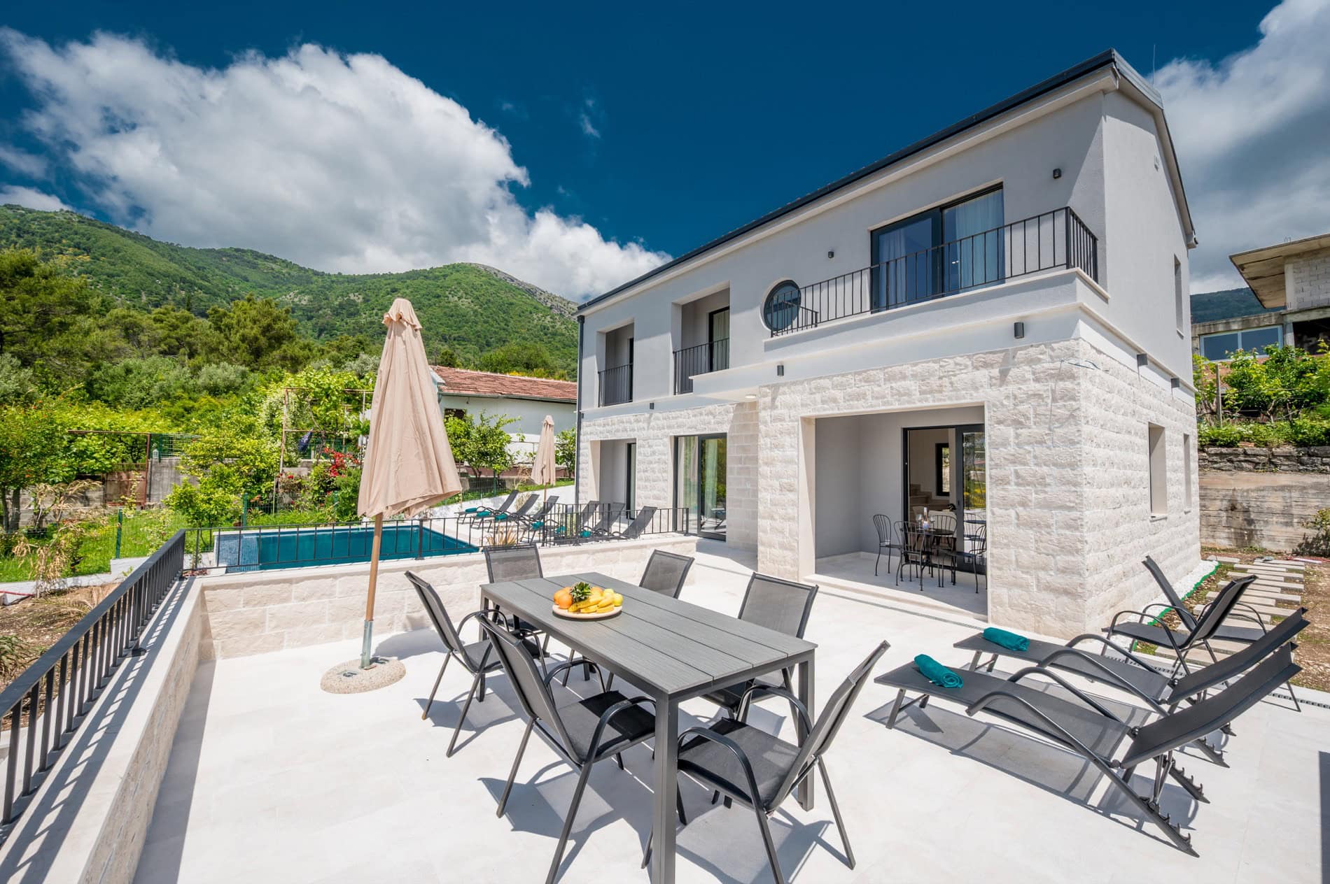 Moderne Villa in Tivat, Montenegro: Terrasse mit Essbereich, Liegestühlen, Pool und Bergblick.