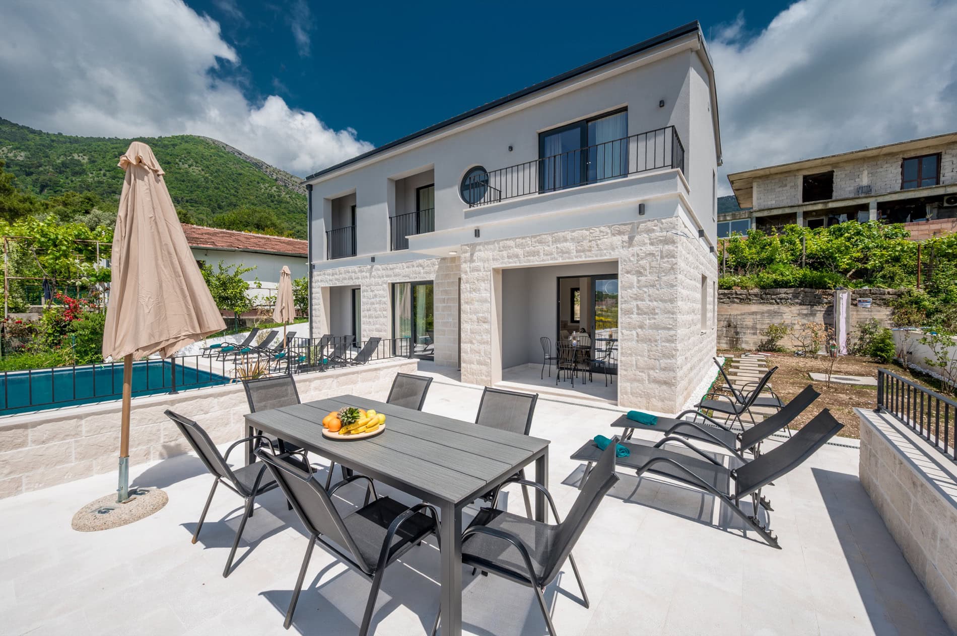 Moderne Villa in Tivat, Montenegro: Terrasse mit Pool, Liegestühlen und Essbereich vor Bergkulisse.