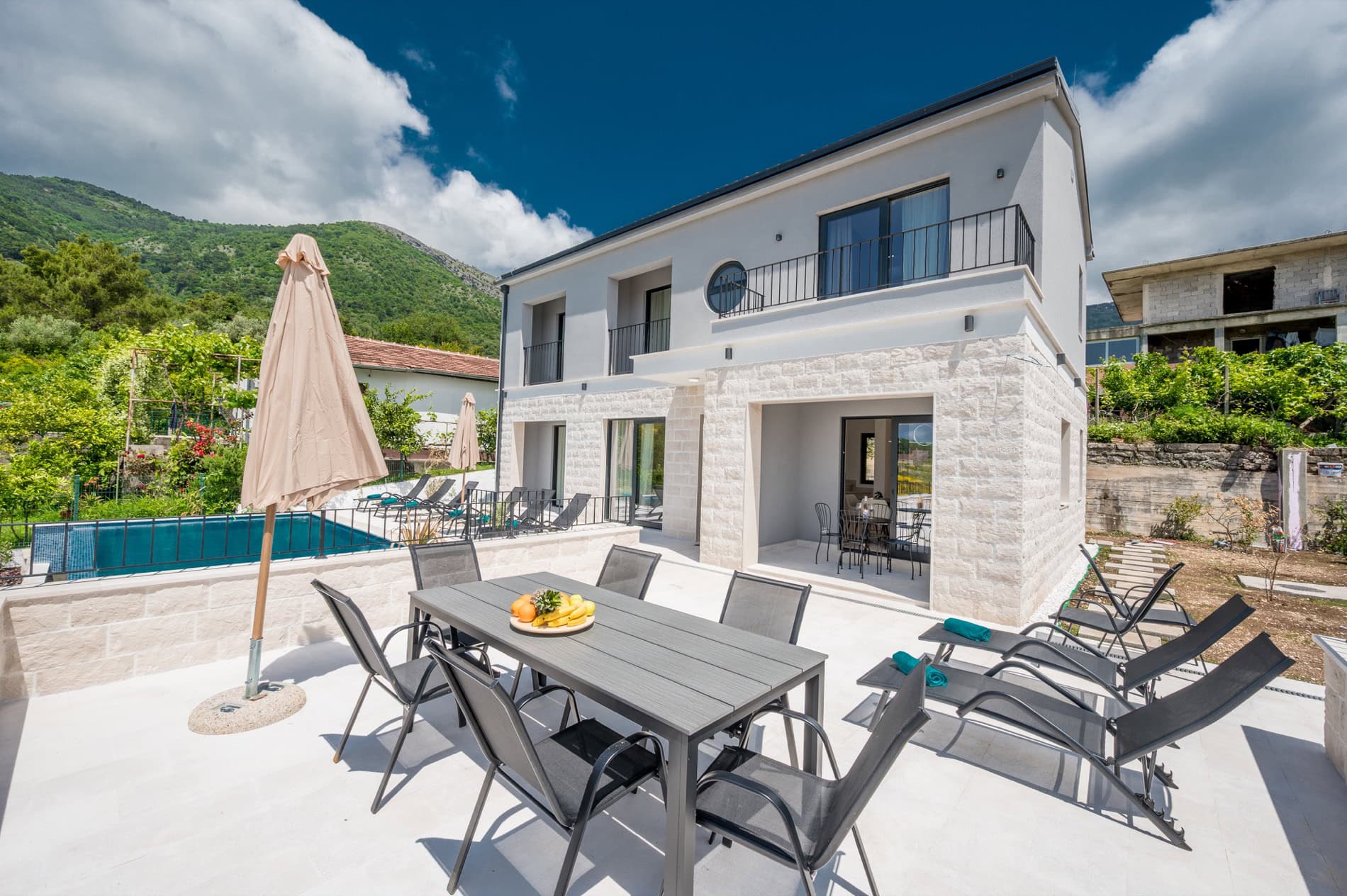Moderne Villa in Tivat, Montenegro: Terrasse mit Essbereich, Liegestühlen, Pool und Bergblick.