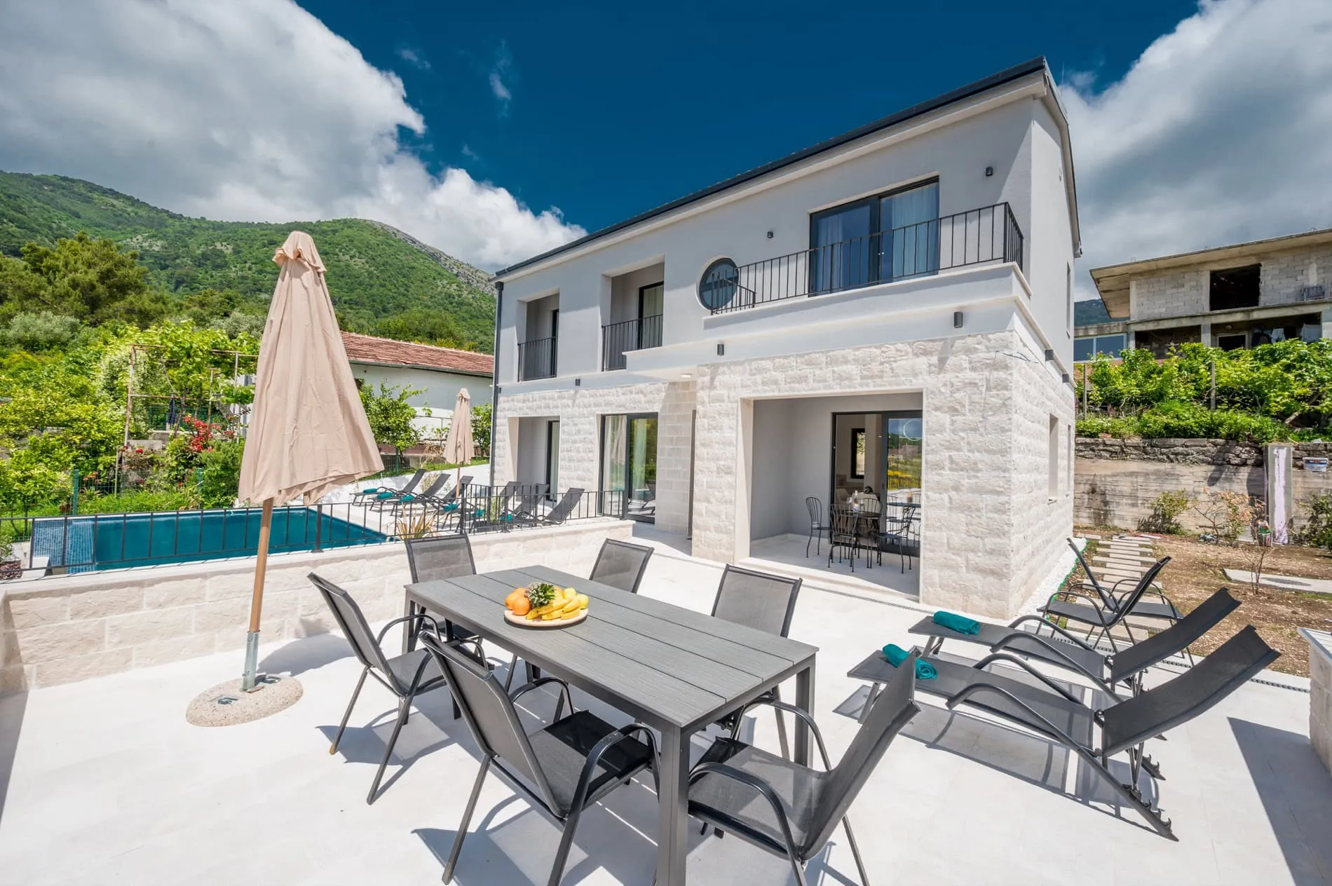 Moderne Villa in Tivat, Montenegro: Terrasse mit Essbereich, Liegestühlen, Pool und Bergblick.