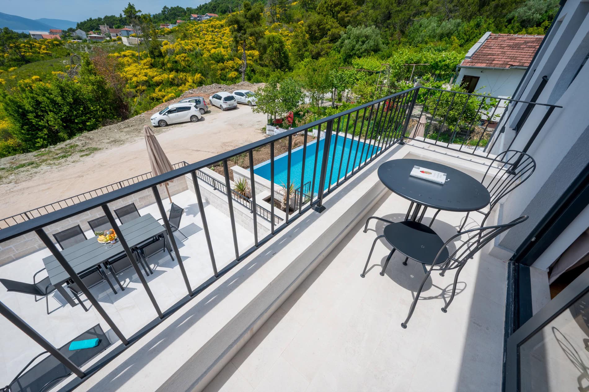 Balkon der Villa in Tivat, Montenegro: Blick auf den Pool, die Terrasse mit Möbeln und die grüne Landschaft mit Parkplatz.
