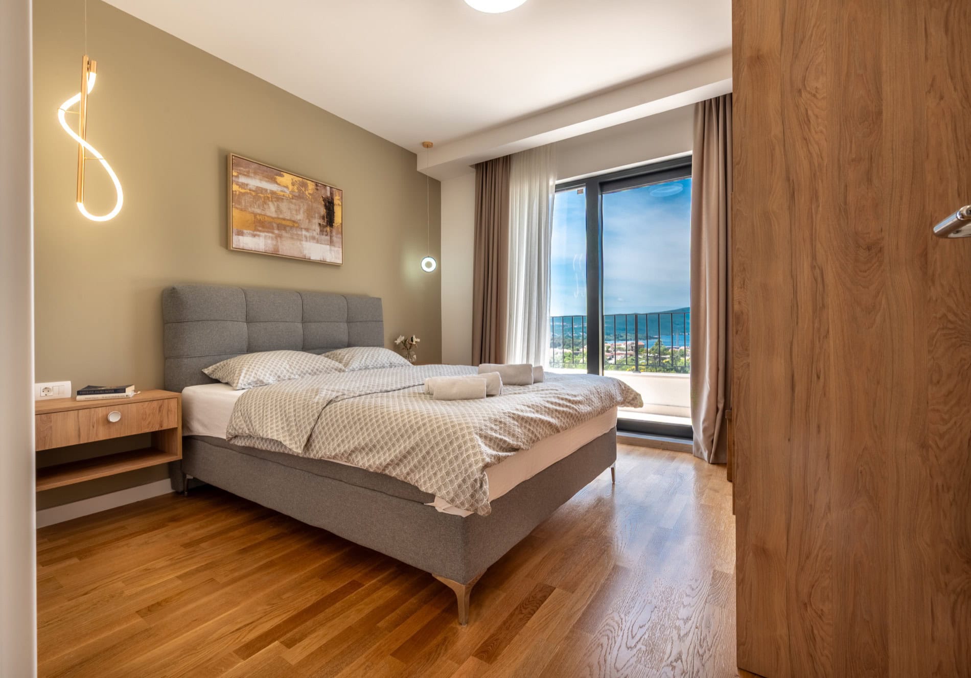 Modernes Schlafzimmer in einer Villa in Tivat, Montenegro: Doppelbett, Parkettboden, Panoramablick auf das Meer aus dem Fenster.