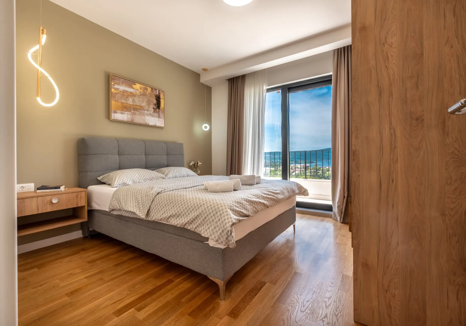 Modernes Schlafzimmer in einer Villa in Tivat, Montenegro: Doppelbett, Parkettboden, Panoramablick auf das Meer aus dem Fenster.