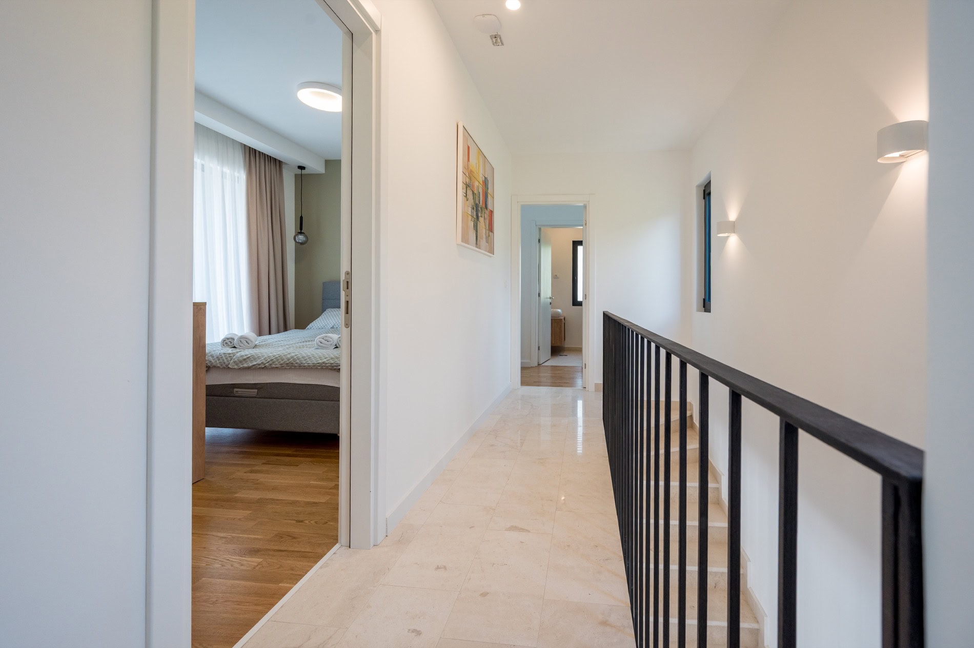 Heller Flur einer Villa in Tivat, Montenegro: Marmorboden, Treppe mit schwarzen Geländern und Eingang zu einem gemütlichen Schlafzimmer.