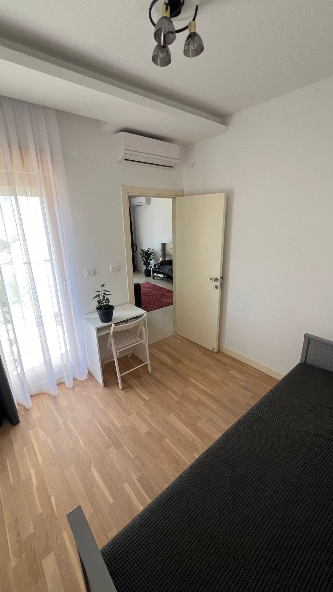 Jasna sypialnia z łóżkiem, biurkiem i wyjściem na balkon w mieszkaniu, miasto Dobrota, Czarnogóra.