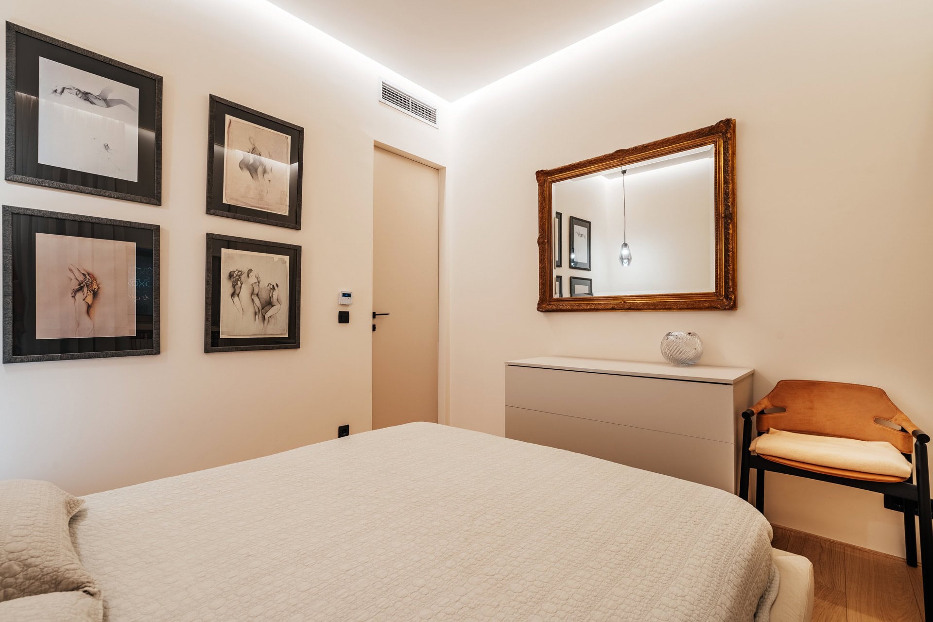 Modernes Schlafzimmer in einer Wohnung in Bečići, Montenegro: helle Möbel, ein Spiegel mit goldenem Rahmen und Bilder an der Wand.
