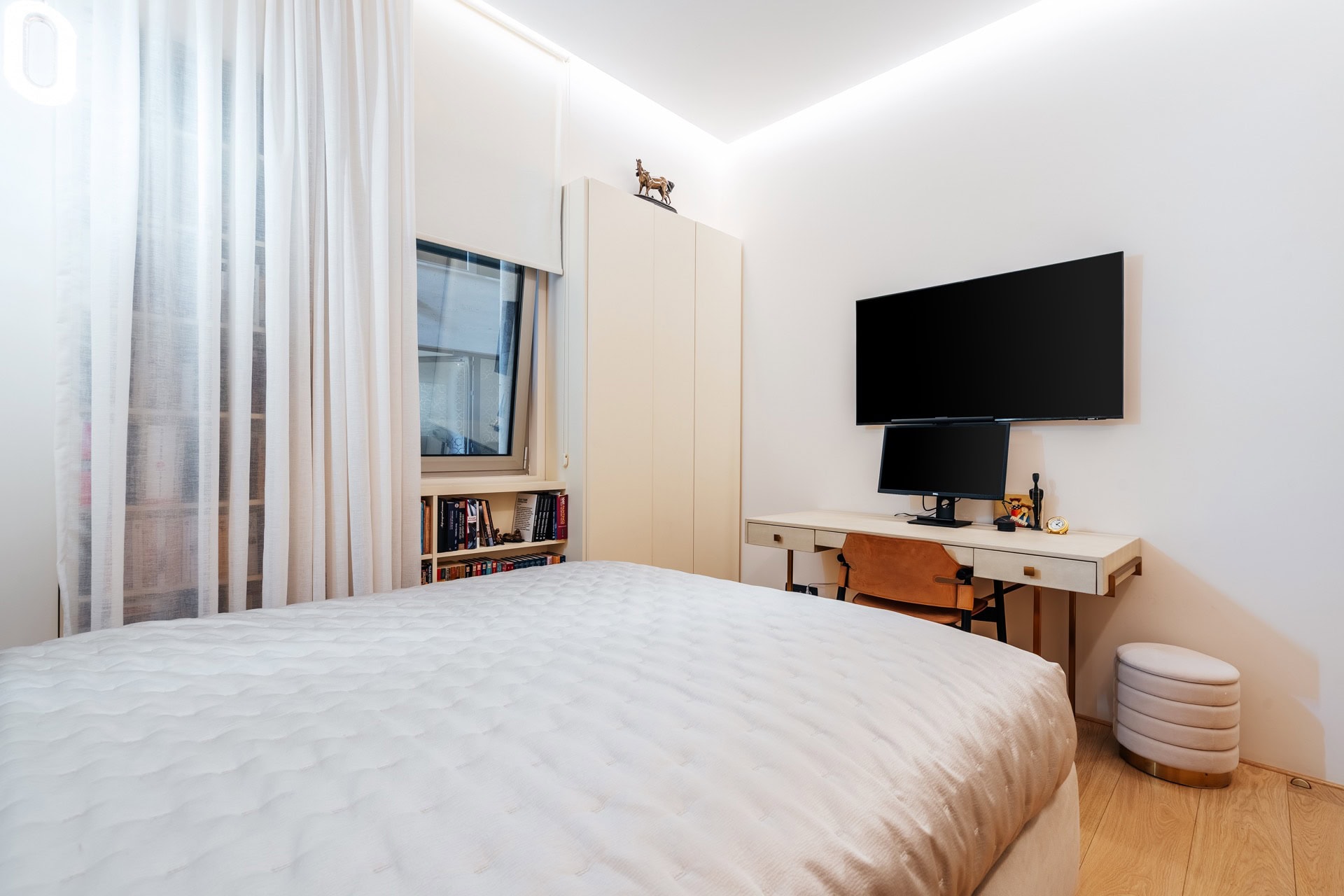 Modernes Schlafzimmer mit Arbeitsbereich und TV in einer Wohnung in Bečići, Montenegro: helle Möbel, Bett und Einbauschrank.