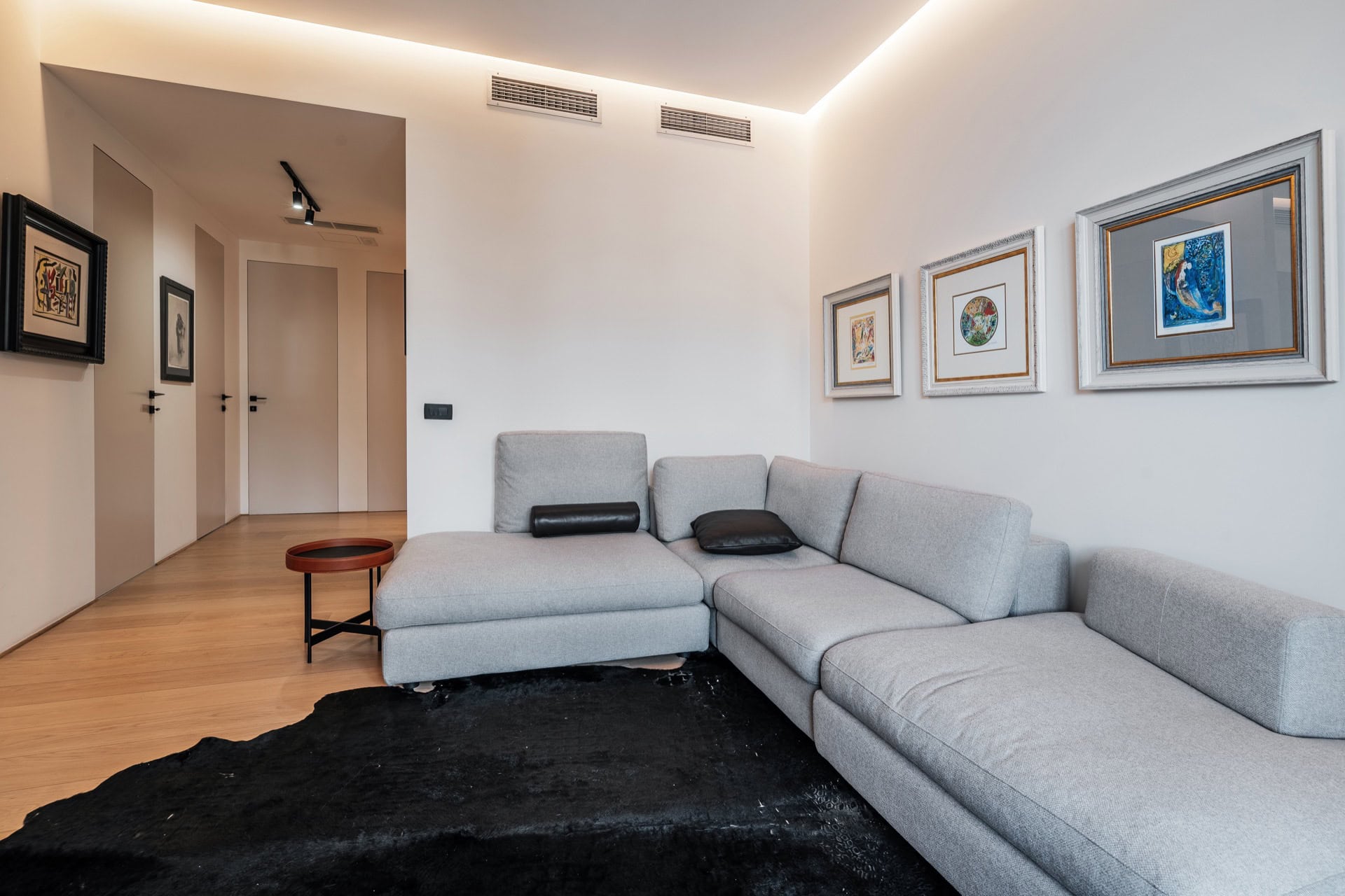Modernes Wohnzimmer mit grauem Sofa in einer Wohnung in Bečići, Montenegro: stilvolles Interieur mit Bildern und indirekter Beleuchtung.