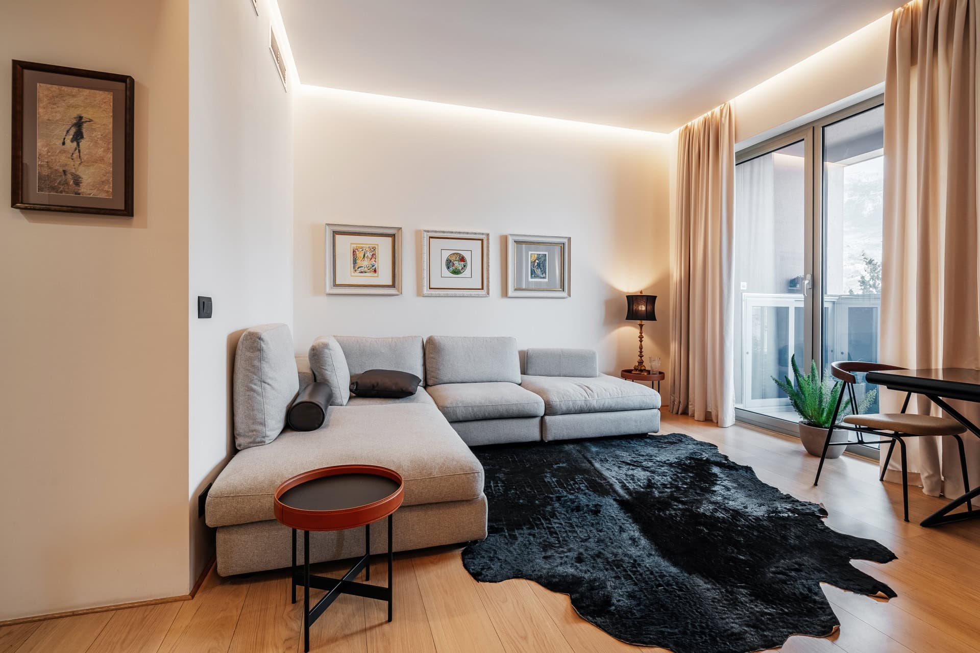 Modernes Wohnzimmer mit grauem Ecksofa und Zugang zum Balkon in einer Wohnung in Bečići, Montenegro.