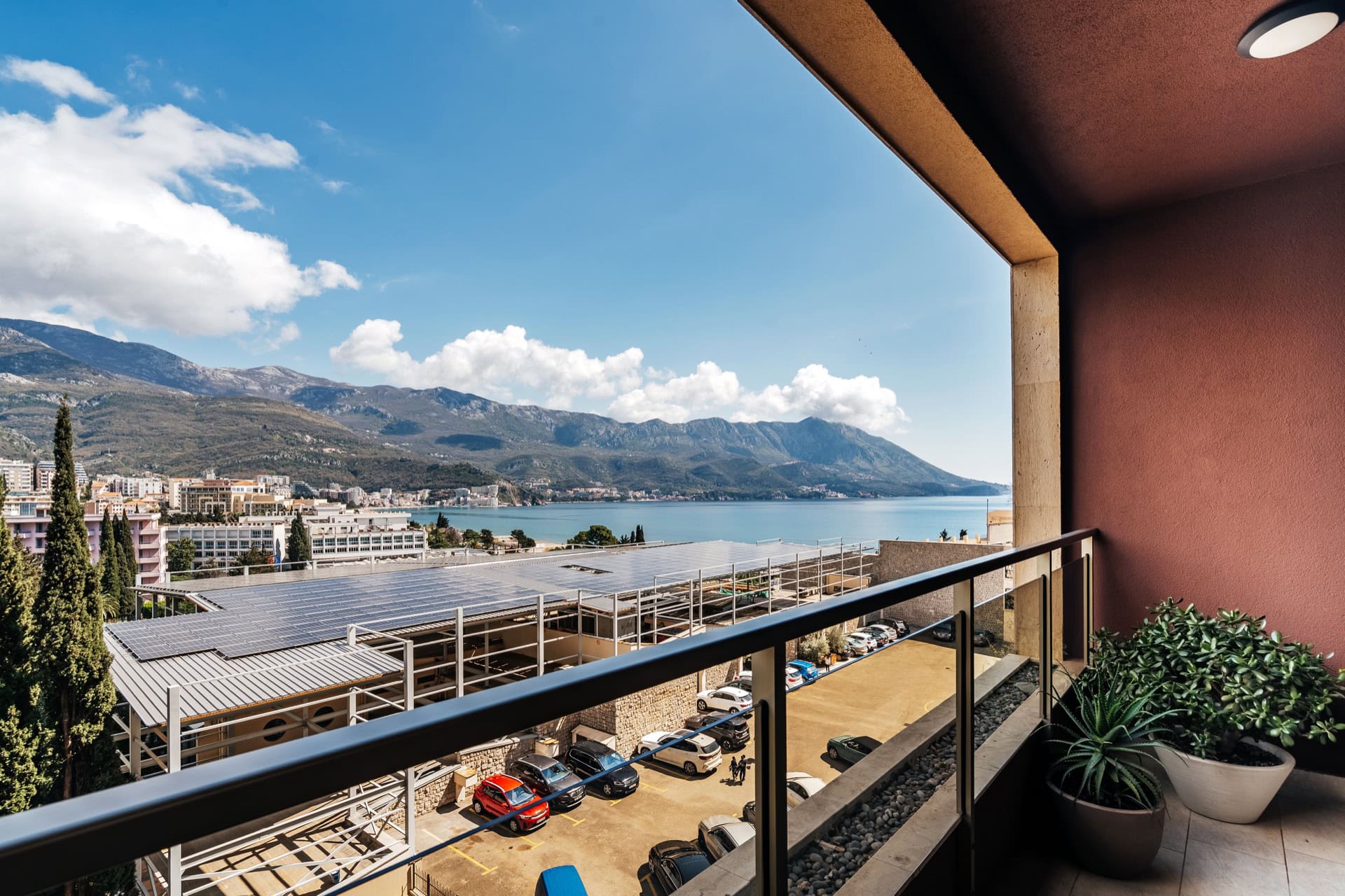 Blick vom Balkon der Wohnung in Bečići, Montenegro: Panorama von Meer, Bergen und Parkplatz mit Solarpaneelen.