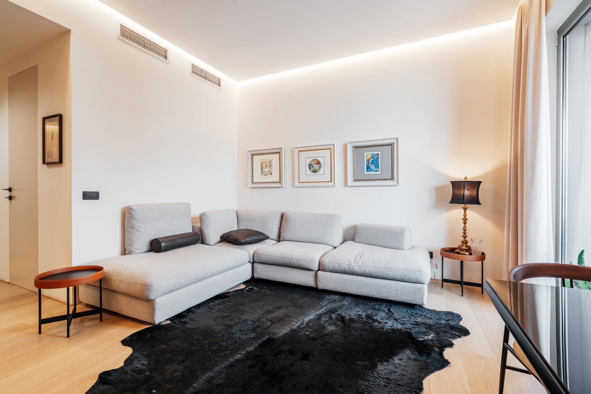 Modernes Wohnzimmer in einer Wohnung in Bečići, Montenegro: graues Ecksofa, schwarzer Teppich und Designerbeleuchtung.