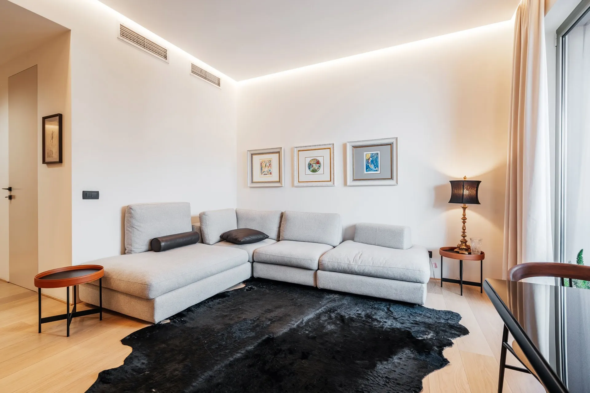 Modernes Wohnzimmer in einer Wohnung in Bečići, Montenegro: graues Ecksofa, schwarzer Teppich und Designerbeleuchtung.