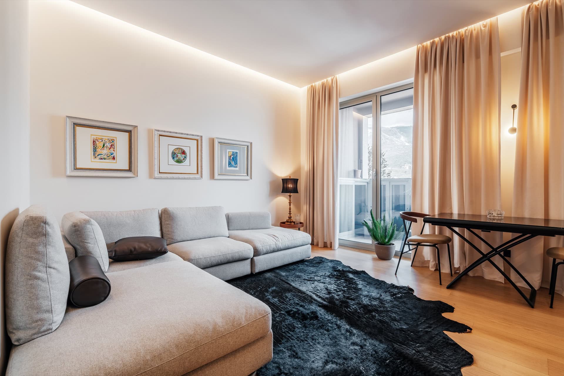Modernes Wohnzimmer in einer Wohnung in Bečići, Montenegro: graues Sofa, schwarzer Teppich, Essbereich und Zugang zum Balkon.