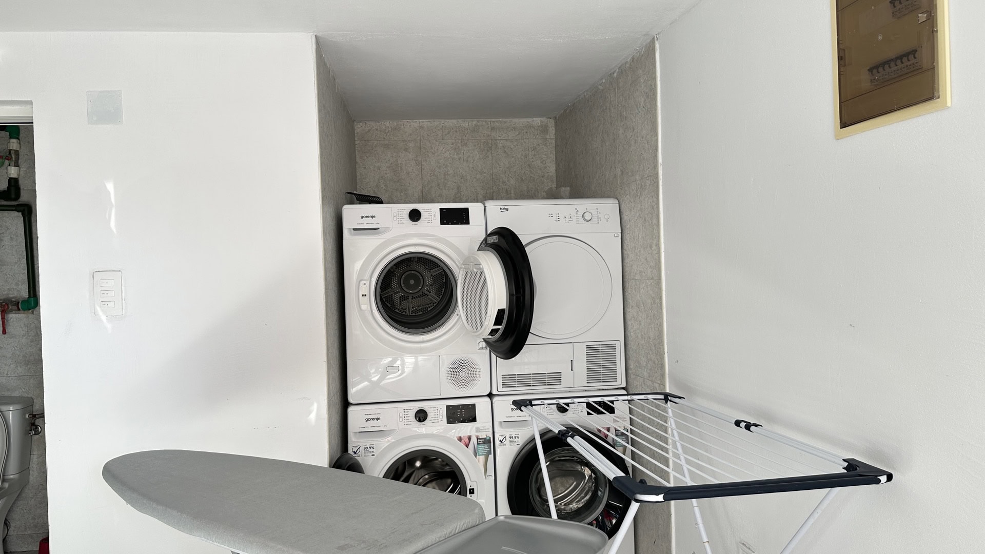 Laundry area in a hotel in Pržno, Montenegro: washing and drying machines, ironing board, and clothes drying rack.