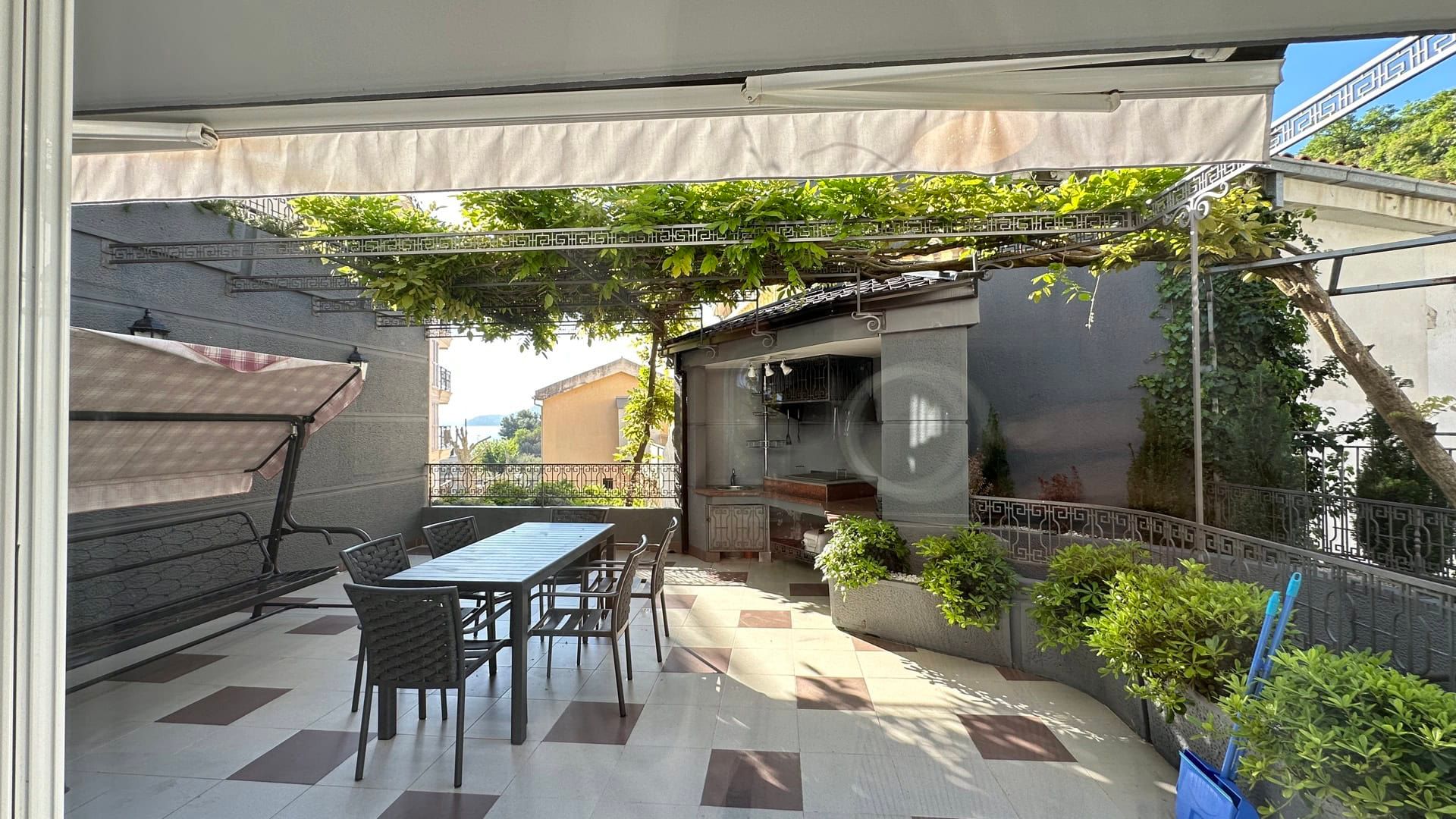 Hotel terrace in Pržno, Montenegro: dining area, garden swing, summer kitchen with grill, and a canopy of greenery.