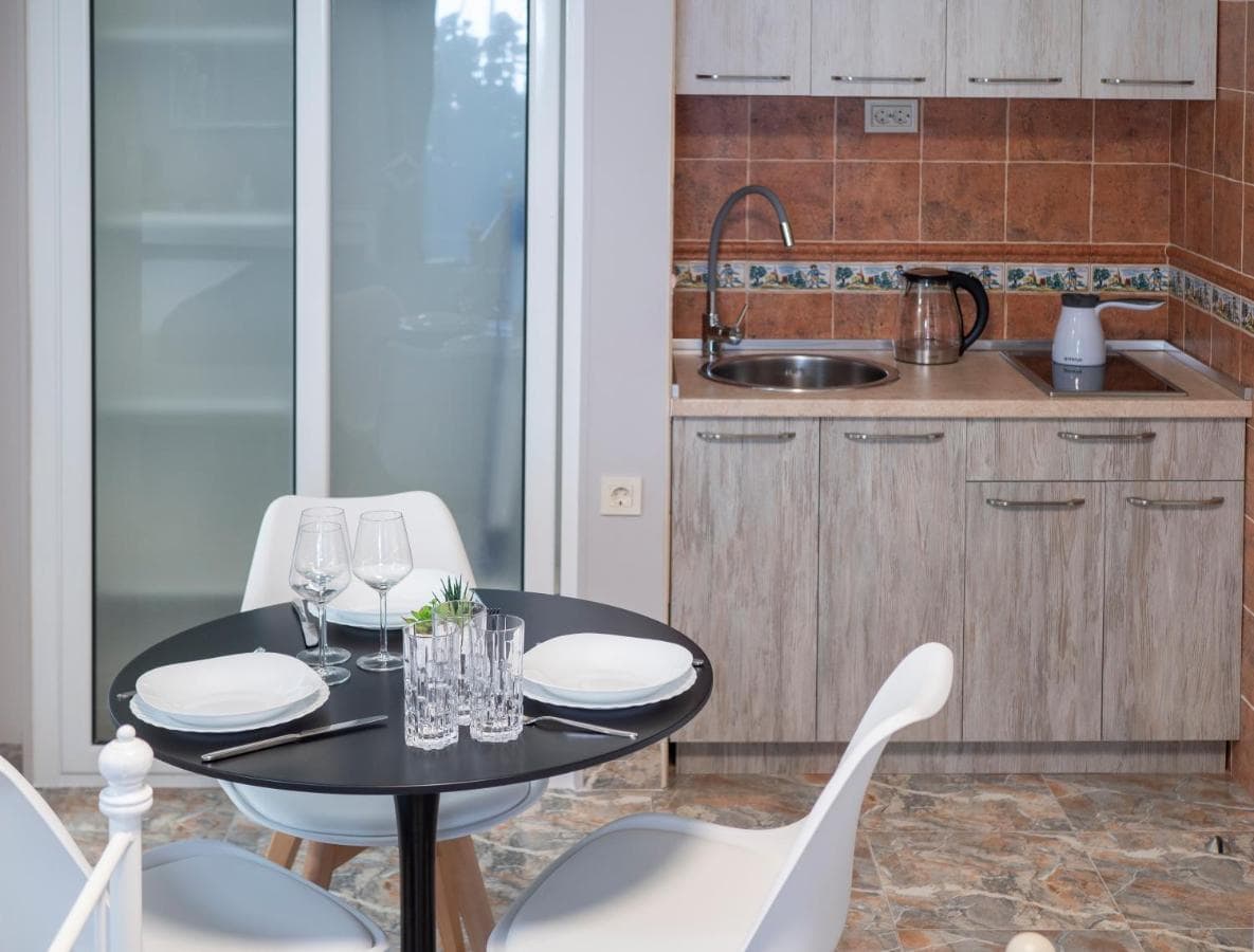 Compact kitchen with dining area in a hotel in Pržno, Montenegro: light-colored cabinets, tile, and a round table with chairs.