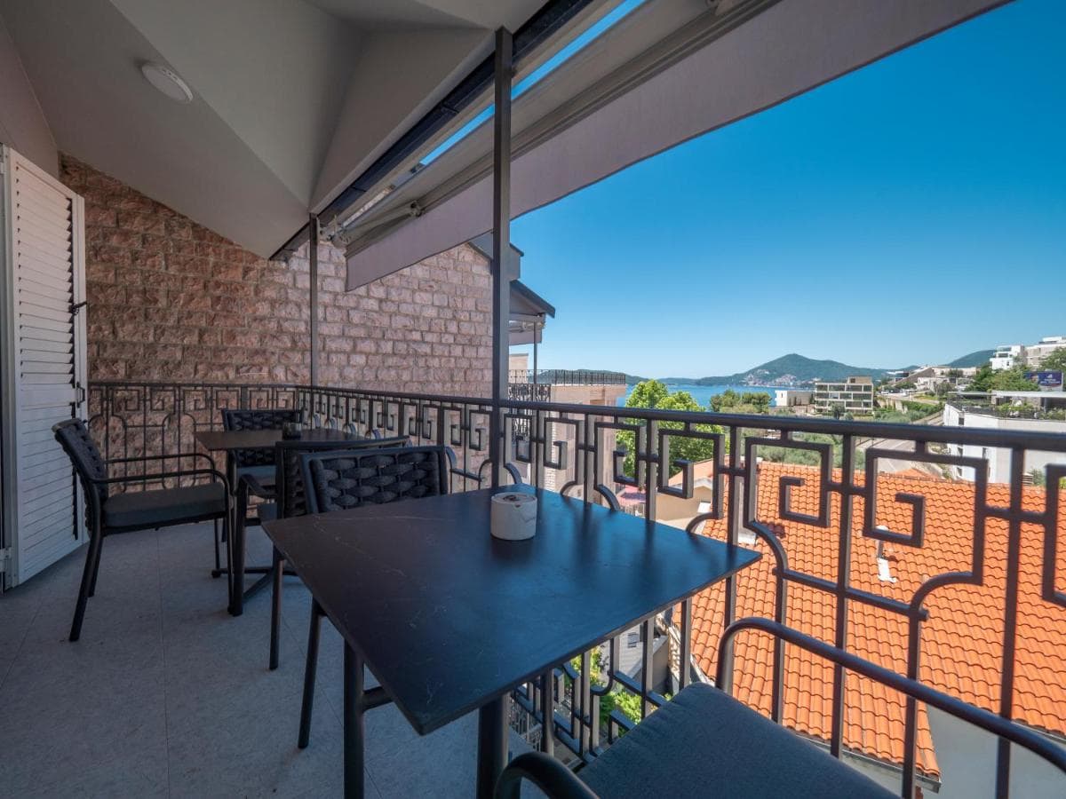 Hotel balcony in Pržno, Montenegro: wrought-iron railings, a table with chairs, and a panoramic view of the sea and mountains.