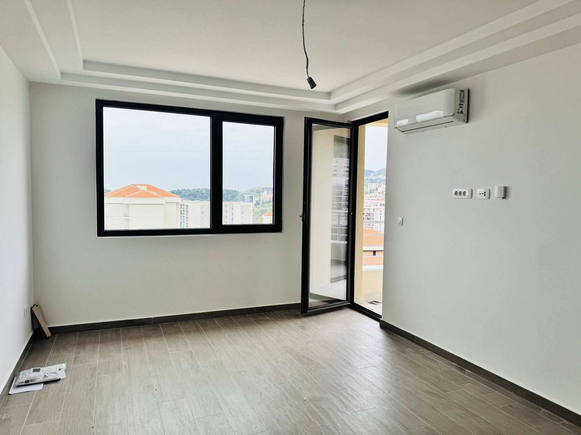 Svetao dnevni boravak u novom stanu u Bečićima, Crna Gora: panoramski prozori, izlaz na balkon, klima-uređaj i pločice.