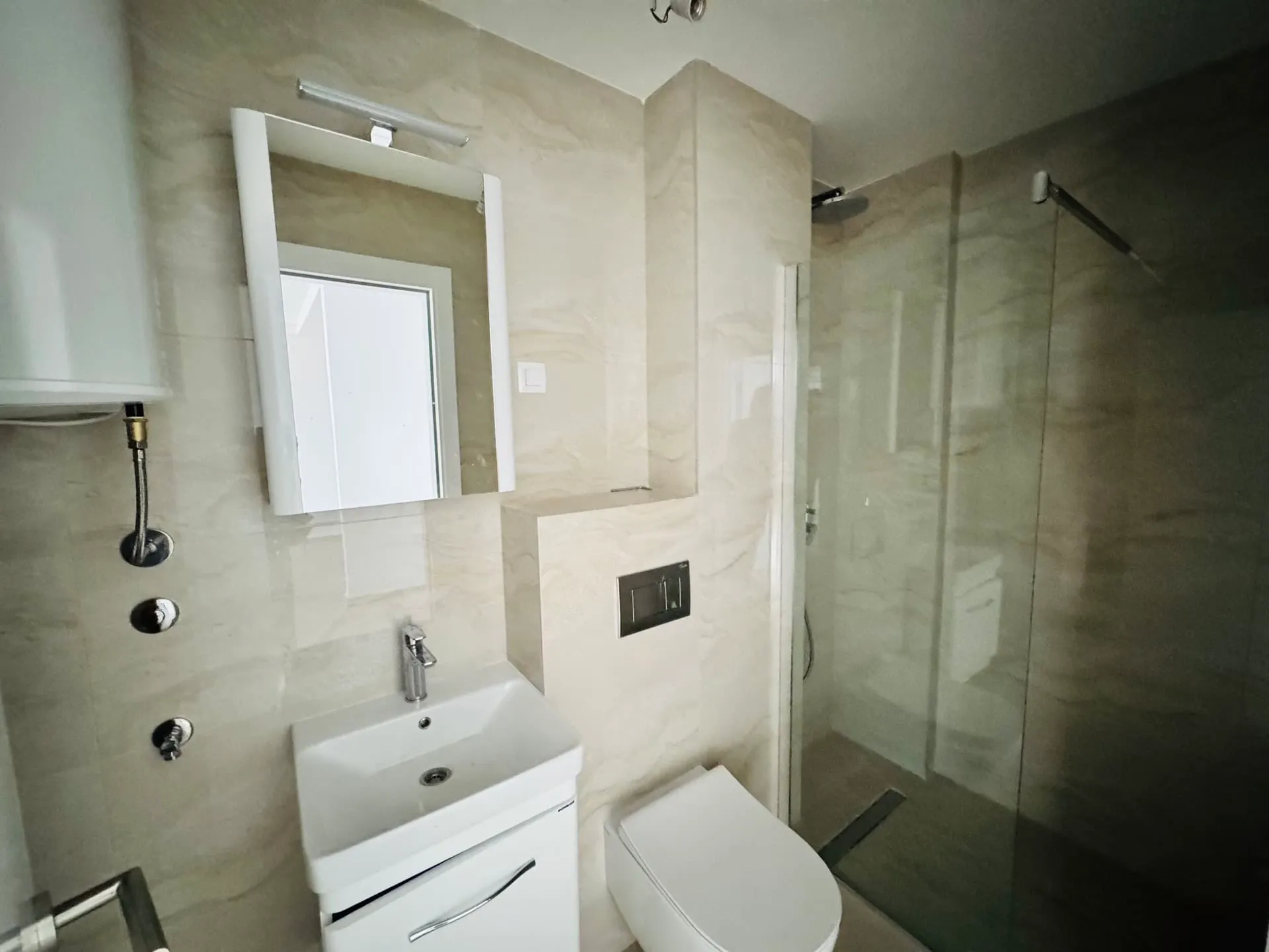 Modernes Badezimmer mit Duschkabine in einer Wohnung, Becici, Montenegro: helle Fliesen, Hänge-WC.