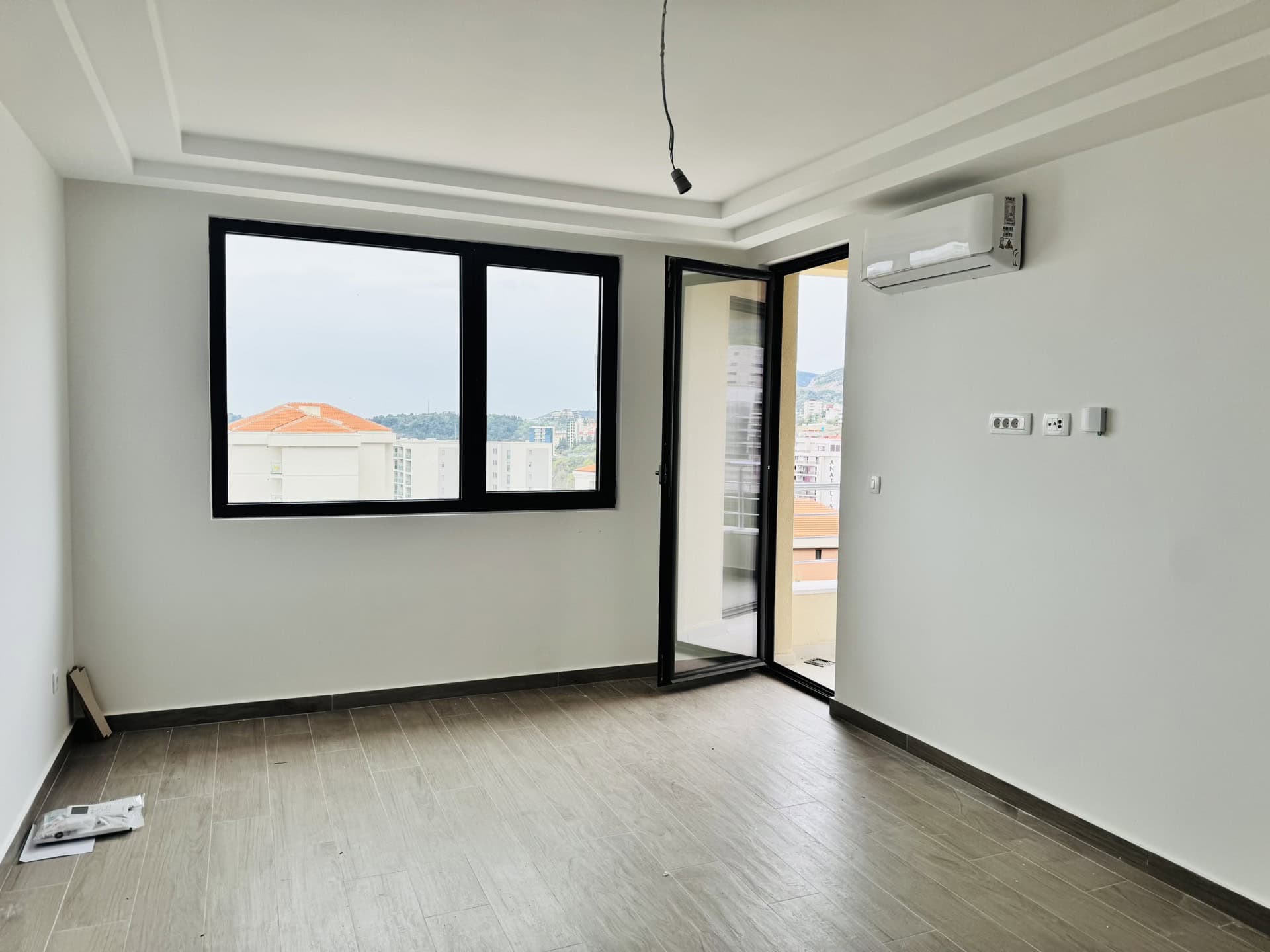 Svetla dnevna soba u novogradnji u Bečićima, Crna Gora: panoramski prozori, izlaz na balkon, klima-uređaj i pločice na podu.