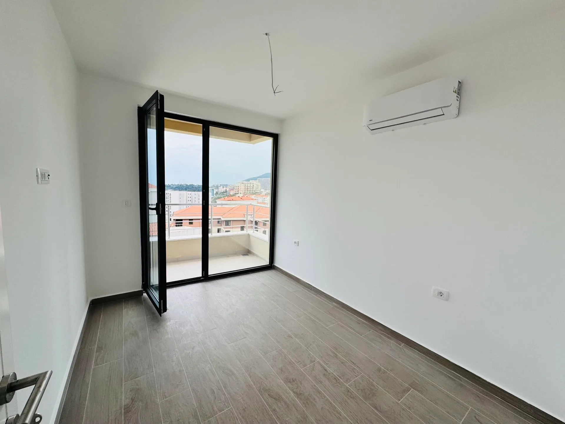Helles Schlafzimmer in einer Wohnung in Bečići, Montenegro: Panoramafenster, Zugang zum Balkon, Klimaanlage und Holzoptik-Fliesen.