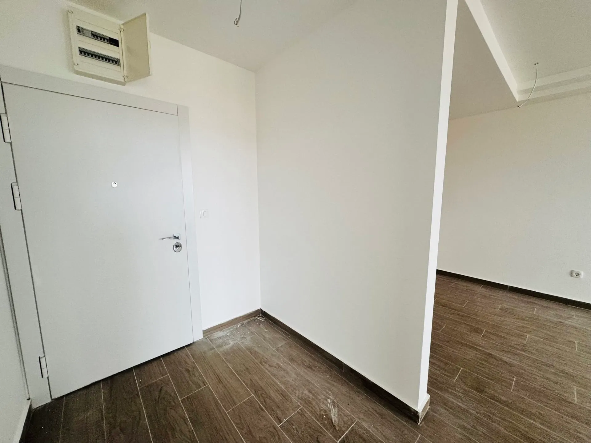 Flur in einer neuen Wohnung in Bečići, Montenegro: weiße Wände, helle Eingangstür und Boden aus Holzoptik-Feinsteinzeug.