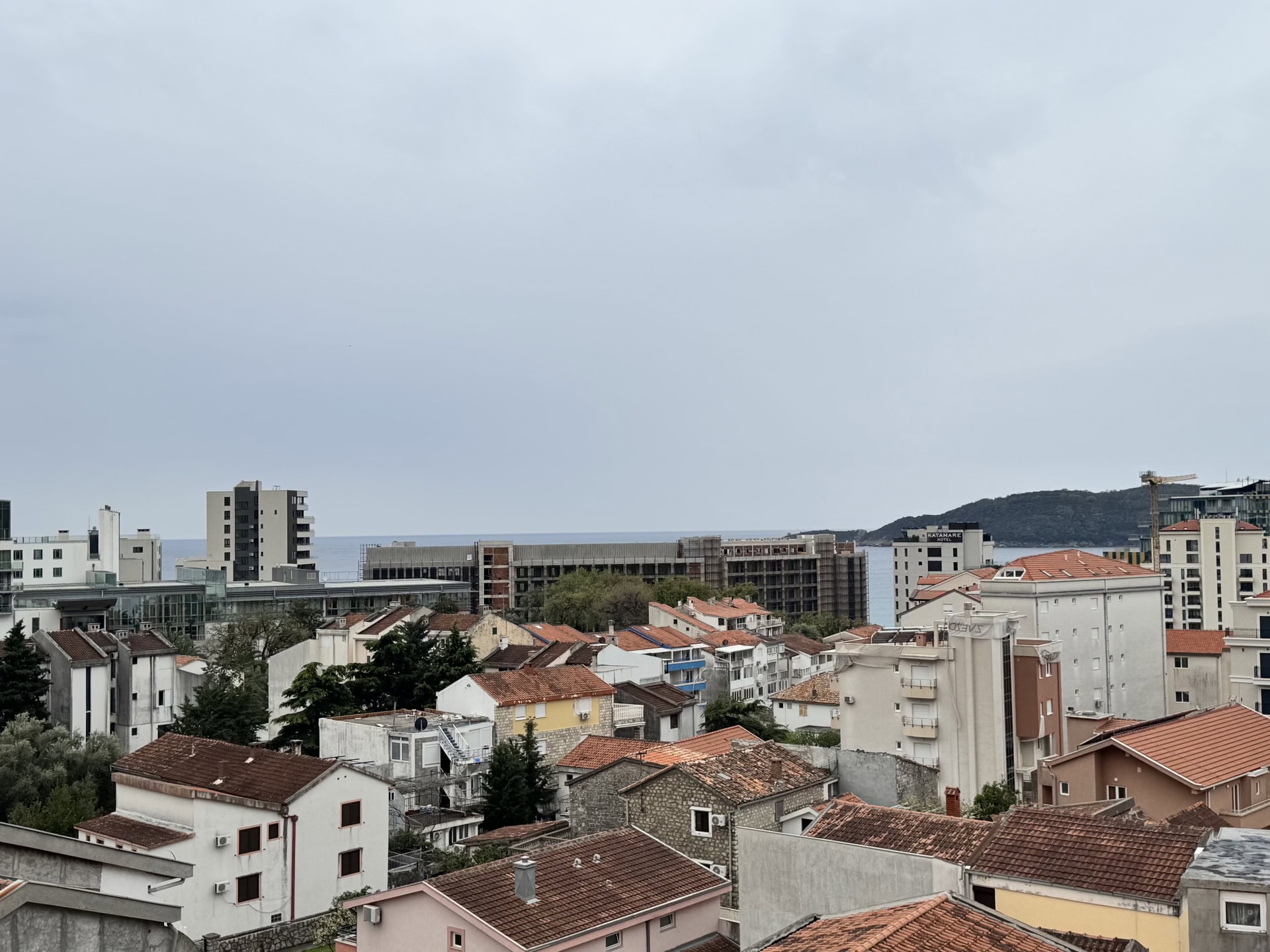 Panoramski pogled na grad Bečići, Crna Gora: stambene zgrade sa krovovima od crepa i morski horizont u daljini.