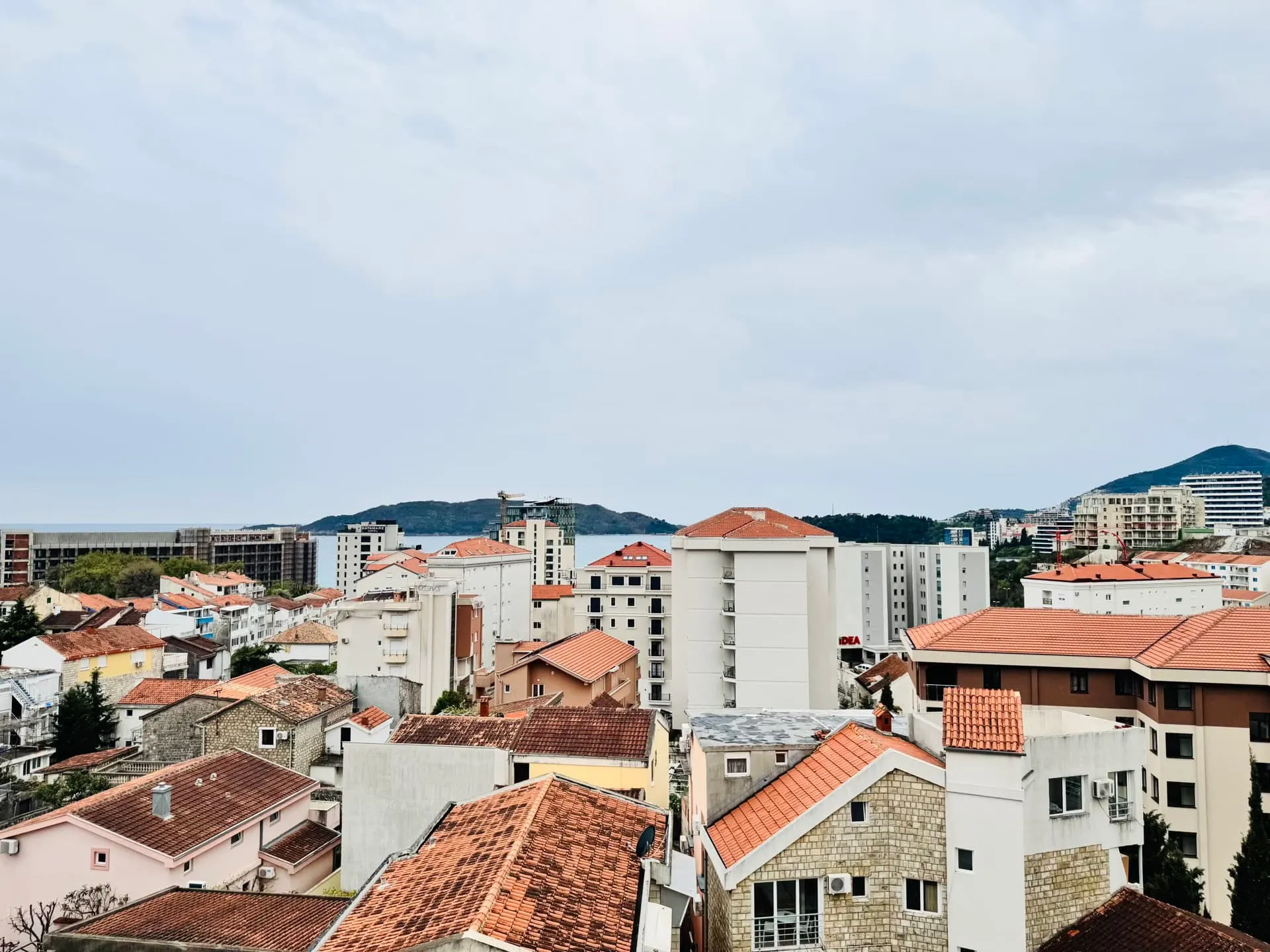 Panoramablick auf die Stadt Bečići, Montenegro, mit roten Ziegeldächern der Häuser und der Küste am Horizont.