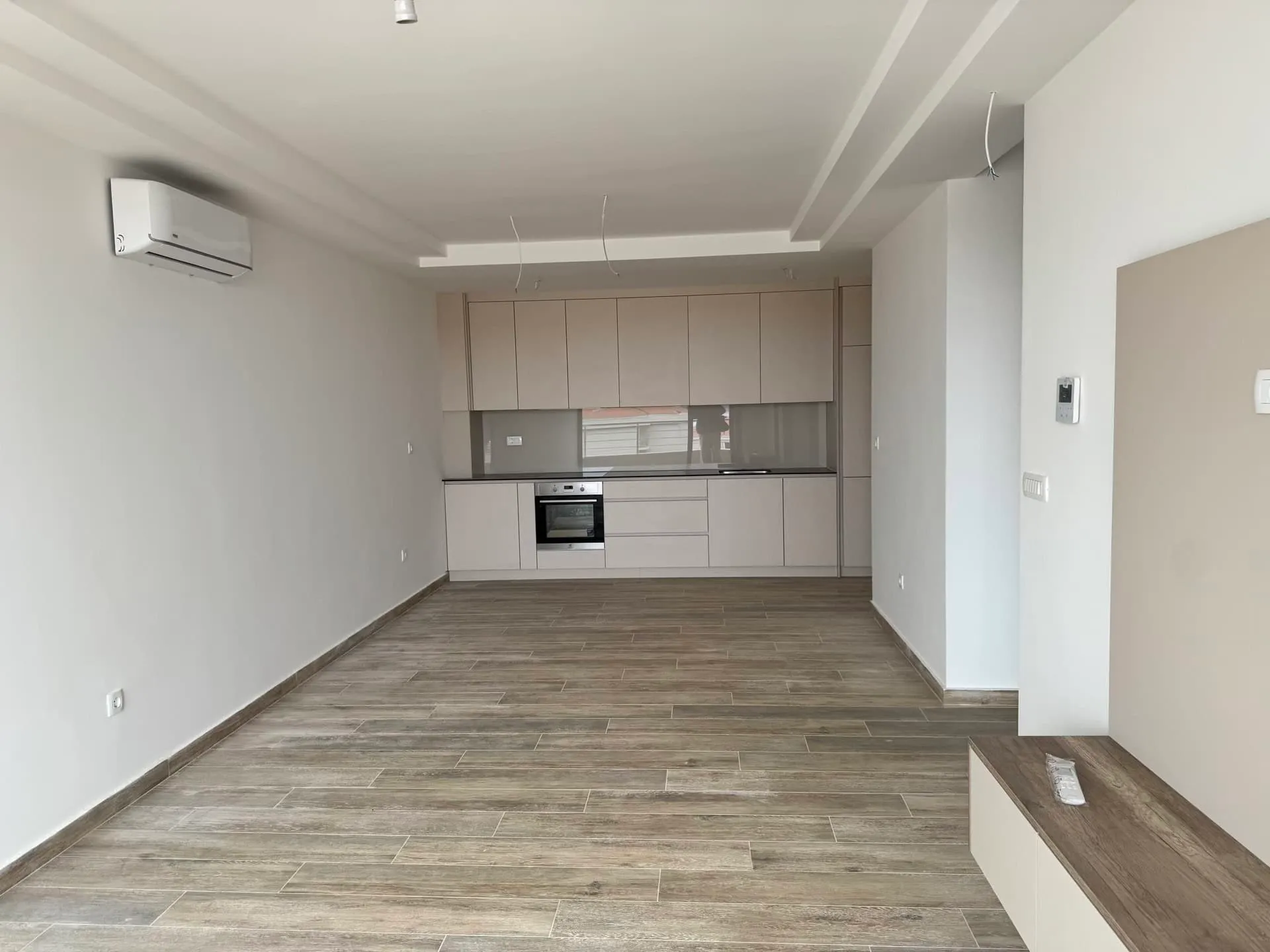 Moderne Wohnküche in einer neuen Wohnung in Bečići, Montenegro: helle Einbauküche, integrierte Geräte und Holzoptik-Fliesen.