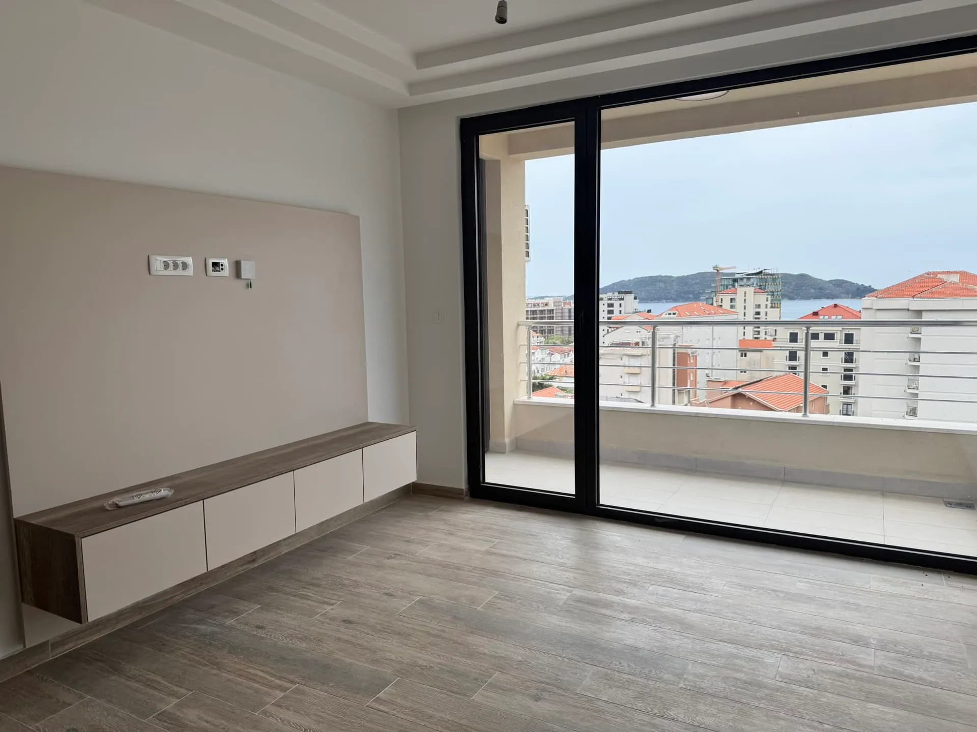 Wohnzimmer in einer Wohnung in Bečići, Montenegro: moderne Ausstattung, hängendes Sideboard und Panoramablick auf das Meer vom Balkon.
