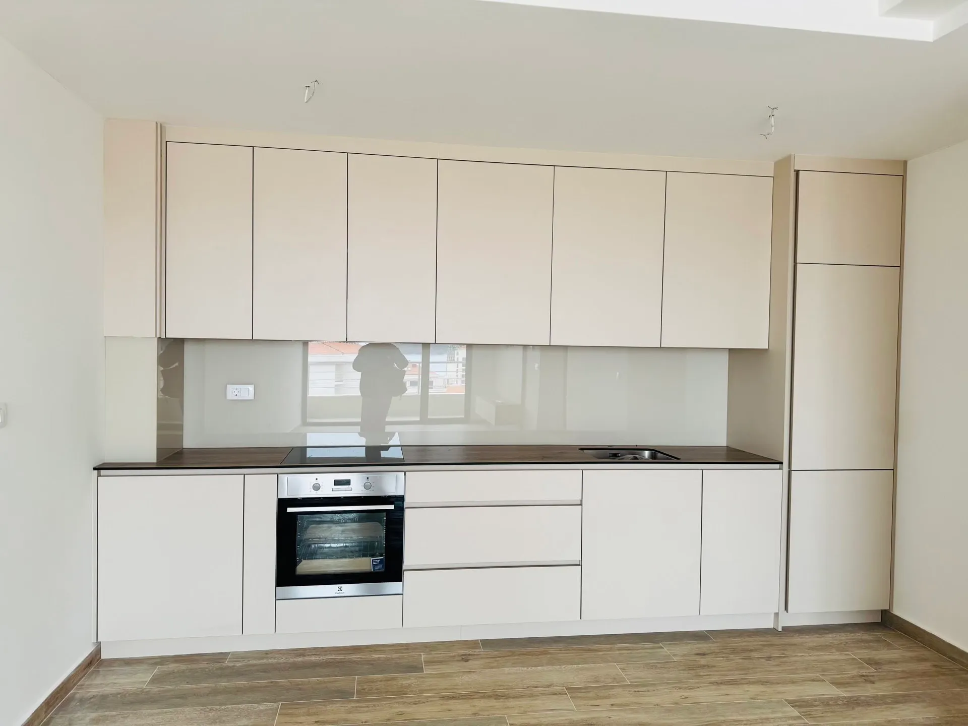 Moderne helle Küche in einer Wohnung in Bečići, Montenegro: Einbaugeräte, matte Fronten und dunkle Arbeitsplatte.