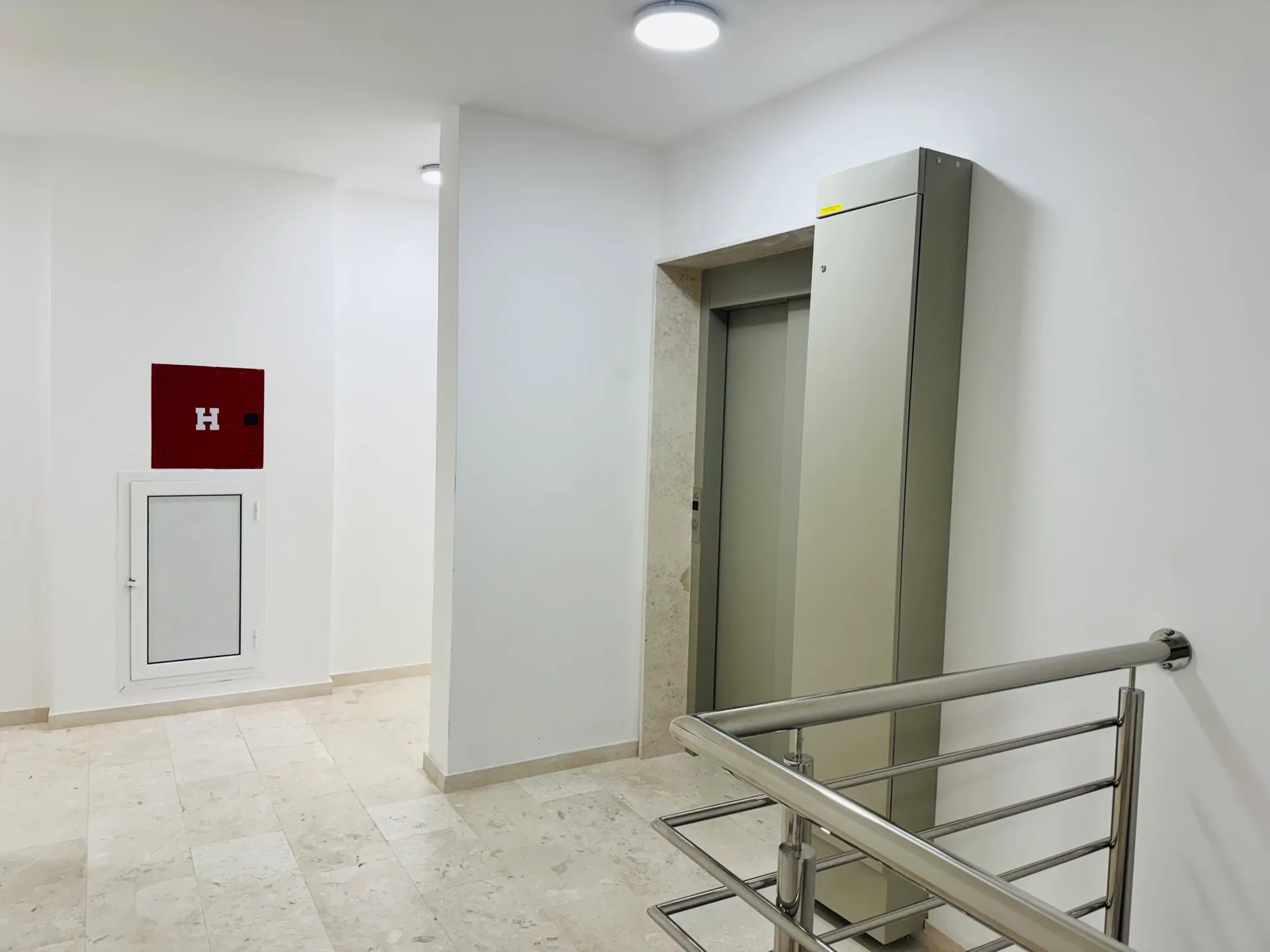 Moderner Aufzugsvorraum in einer Wohnanlage in Bečići, Montenegro: helle Ausstattung, Fliesen und Metallgeländer.