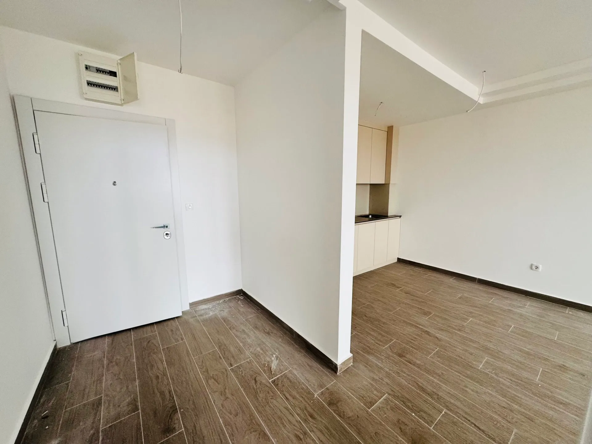 Wohnzimmer mit Küchenbereich in einer neuen Wohnung in Bečići, Montenegro: helle Ausstattung, Holzoptik-Fliesen, Eingangstür.