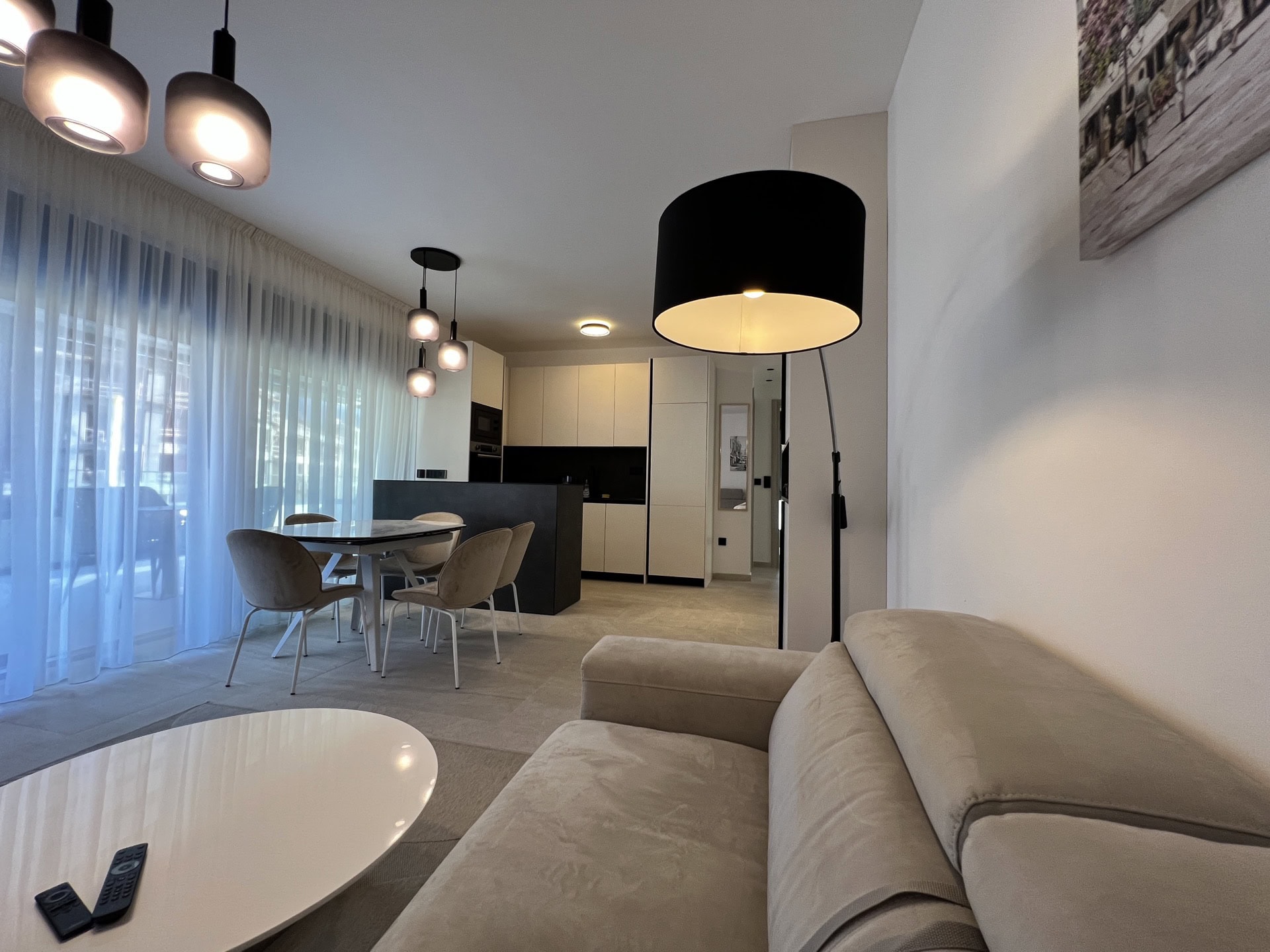 Savremeni dnevni boravak sa kuhinjom u stanu u Tivtu, Crna Gora: svetla sofa, trpezarijski deo i stilizovano osvetljenje.