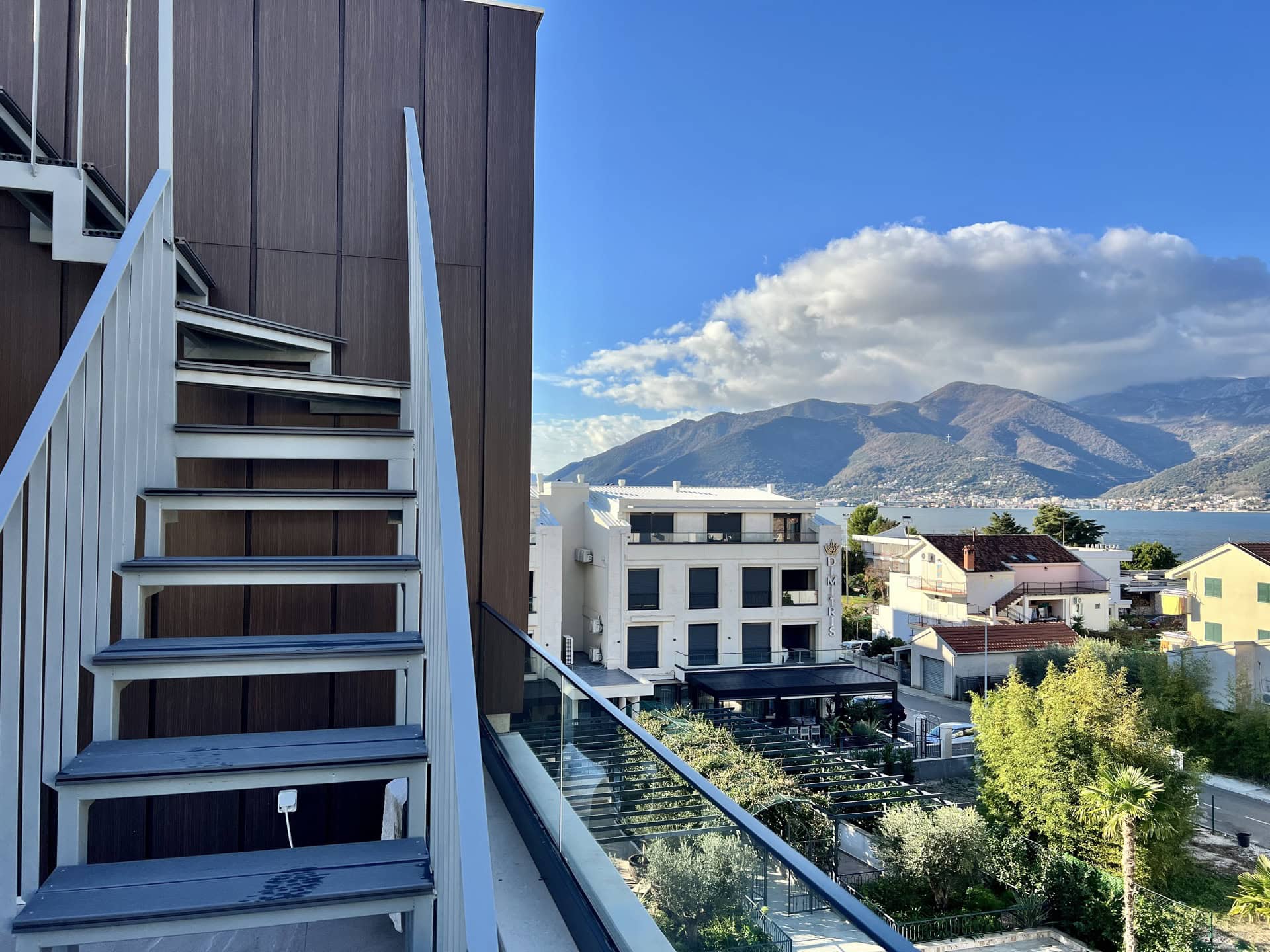 Pogled sa balkona stana u Tivtu, Crna Gora: moderno stepenište, panoramski pogled na more i planine Bokokotorskog zaliva.