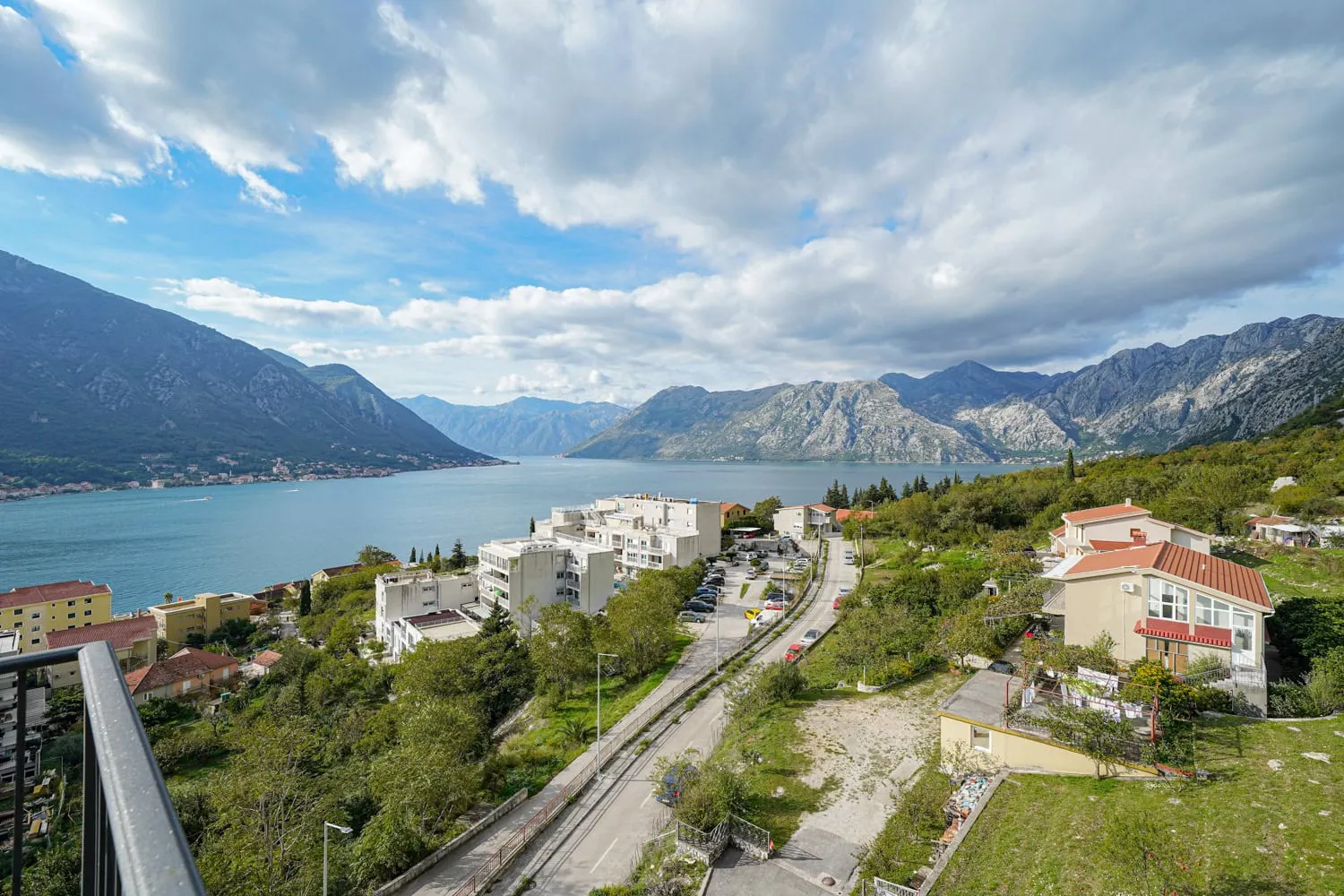 Panoramablick auf die Bucht von Kotor und die Berge aus einer Wohnung in Dobrota, Montenegro: Wohngebiet, Straße und Meereslandschaft.