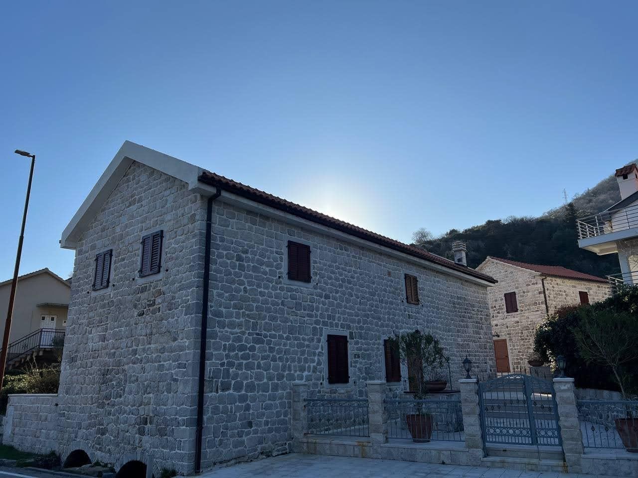 Traditional stone villa in Kamenari, Montenegro: natural stone facade, tiled roof, and wrought-iron fence.
