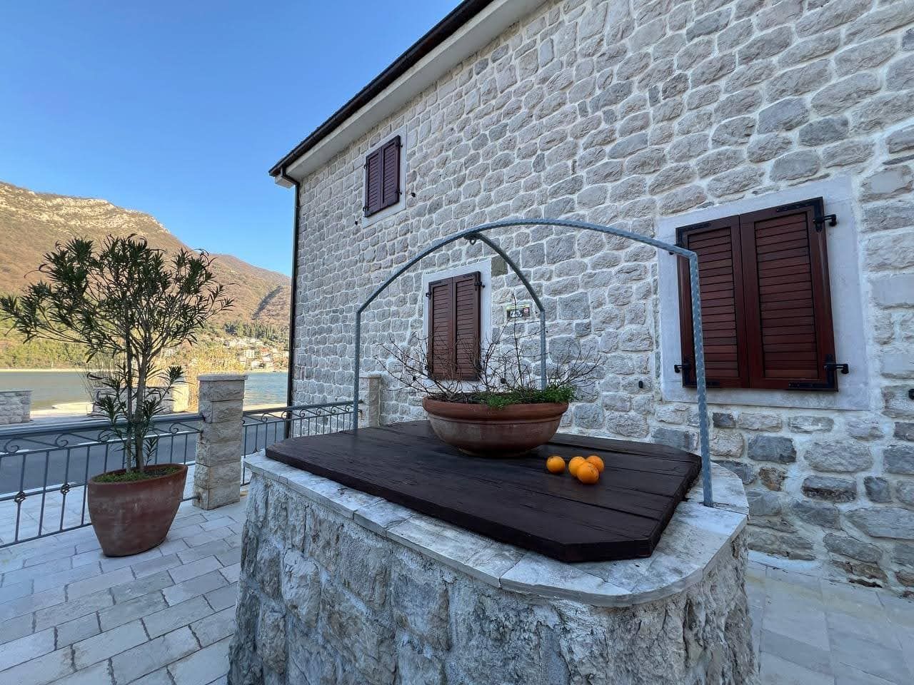 Stone facade of a villa in Kamenari, Montenegro, with a decorative well, terrace, and sea and mountain views.
