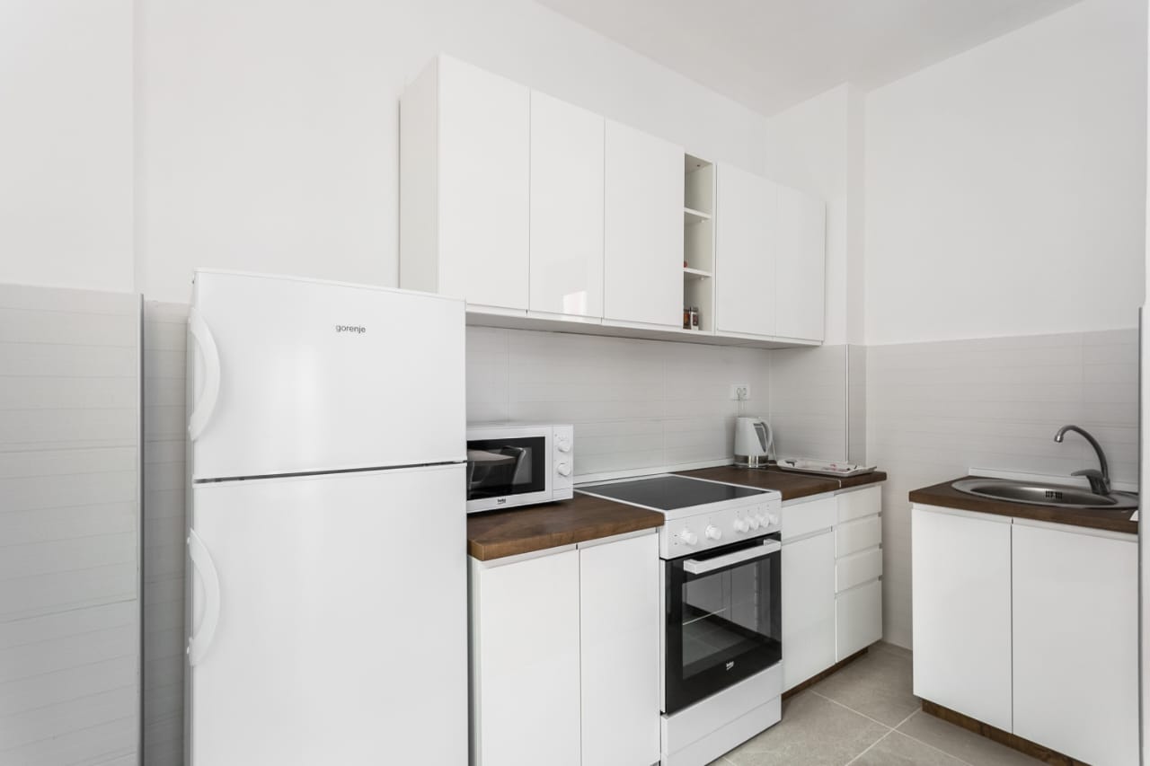 Современная белая кухня с техникой Gorenje в квартире в Будве, Черногория: встроенная плита и холодильник.