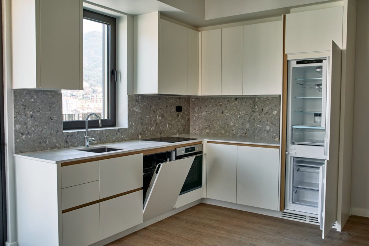 Moderne weiße Küche mit Steinspritzschutz und Einbaugeräten in einer Wohnung in Tivat, Montenegro.